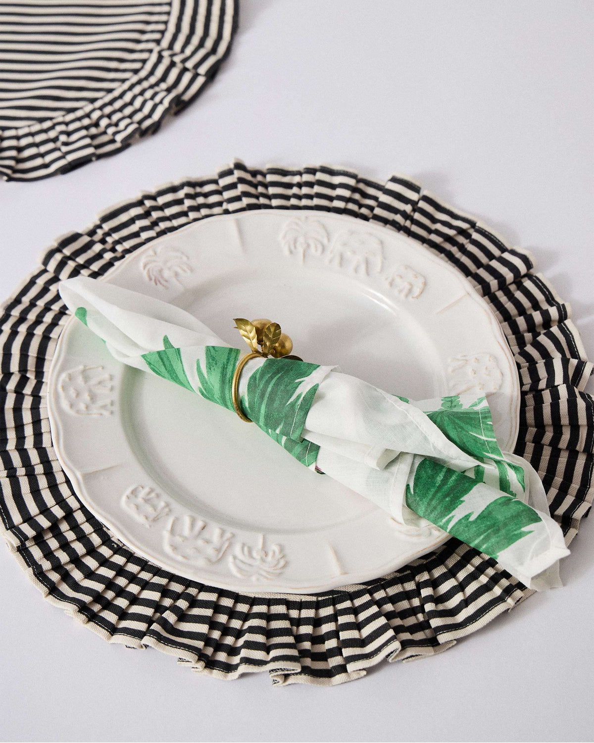 Ceylon Trail palm napkin on a plate over a striped placemat.