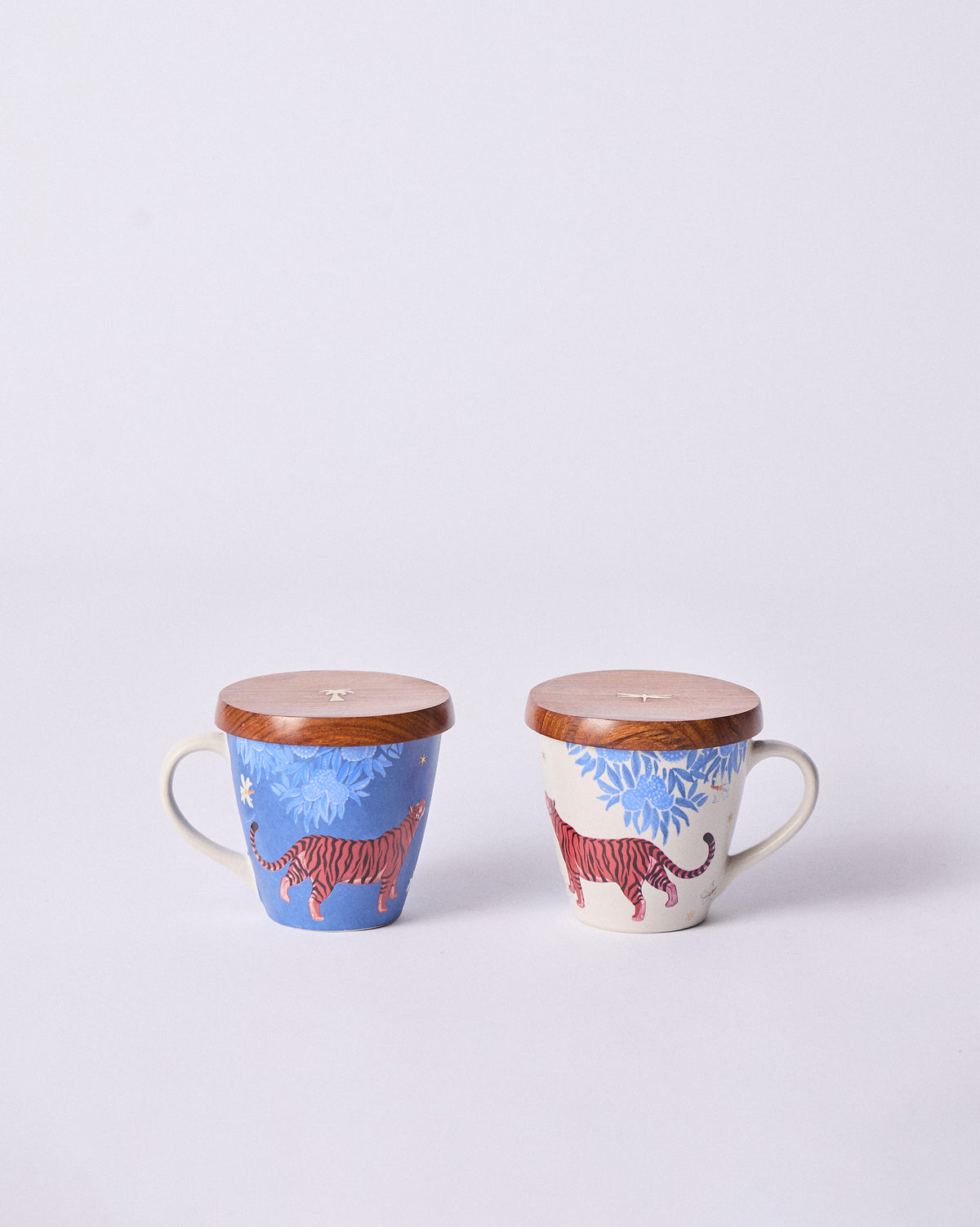 Blue and cream Nadi mugs with red tigers, each topped with a wooden lid.