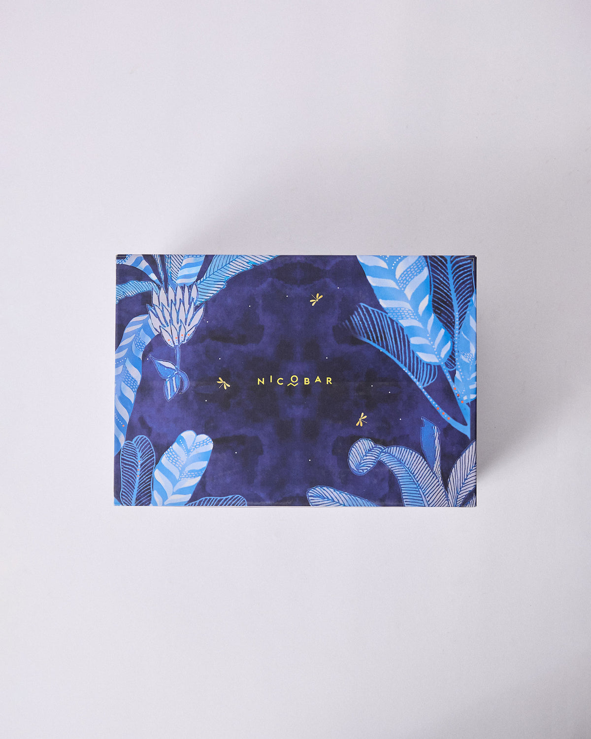 Navy Nadi gift box lid with tropical leaves, gold dragonflies, and Nicobar branding.