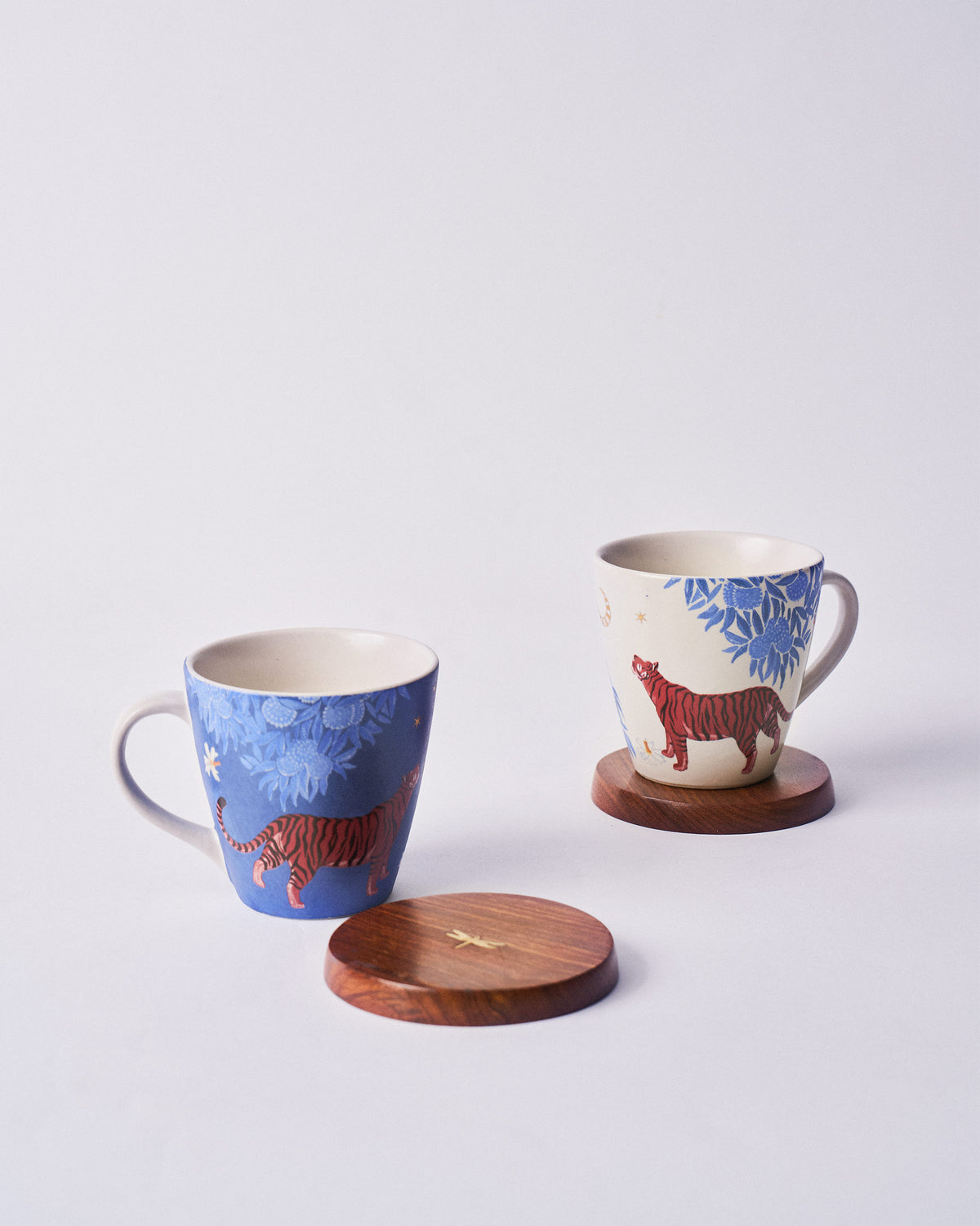 Blue and cream Nadi mugs with red tiger prints beside a wooden dragonfly lid.