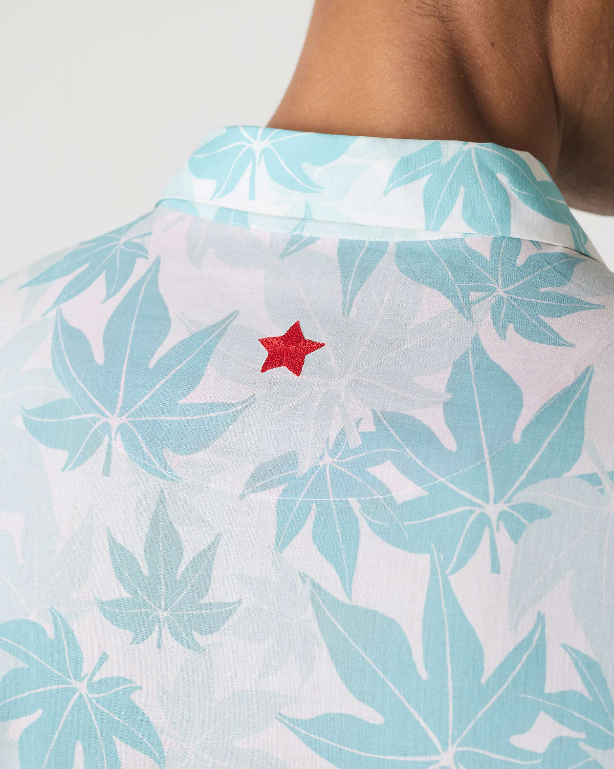 Close-up of the Mistari shirt back showing a red embroidered star on the leaf print.