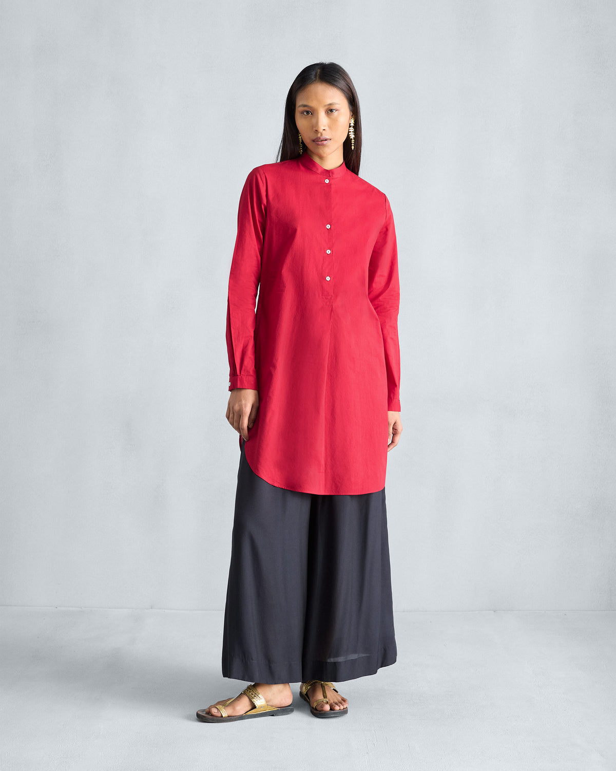Person wearing a red mid-length kurta with buttoned cuffs.