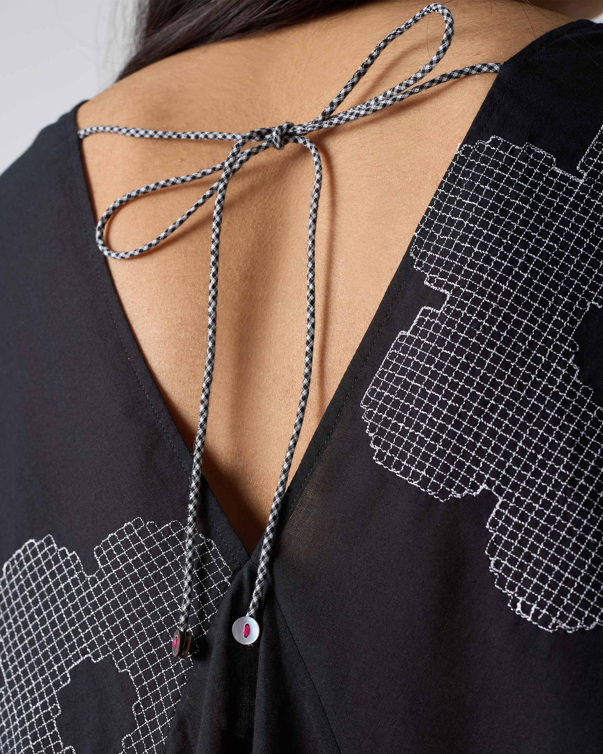 Close-up of a black Curved Hem Top back with a checkered tie.