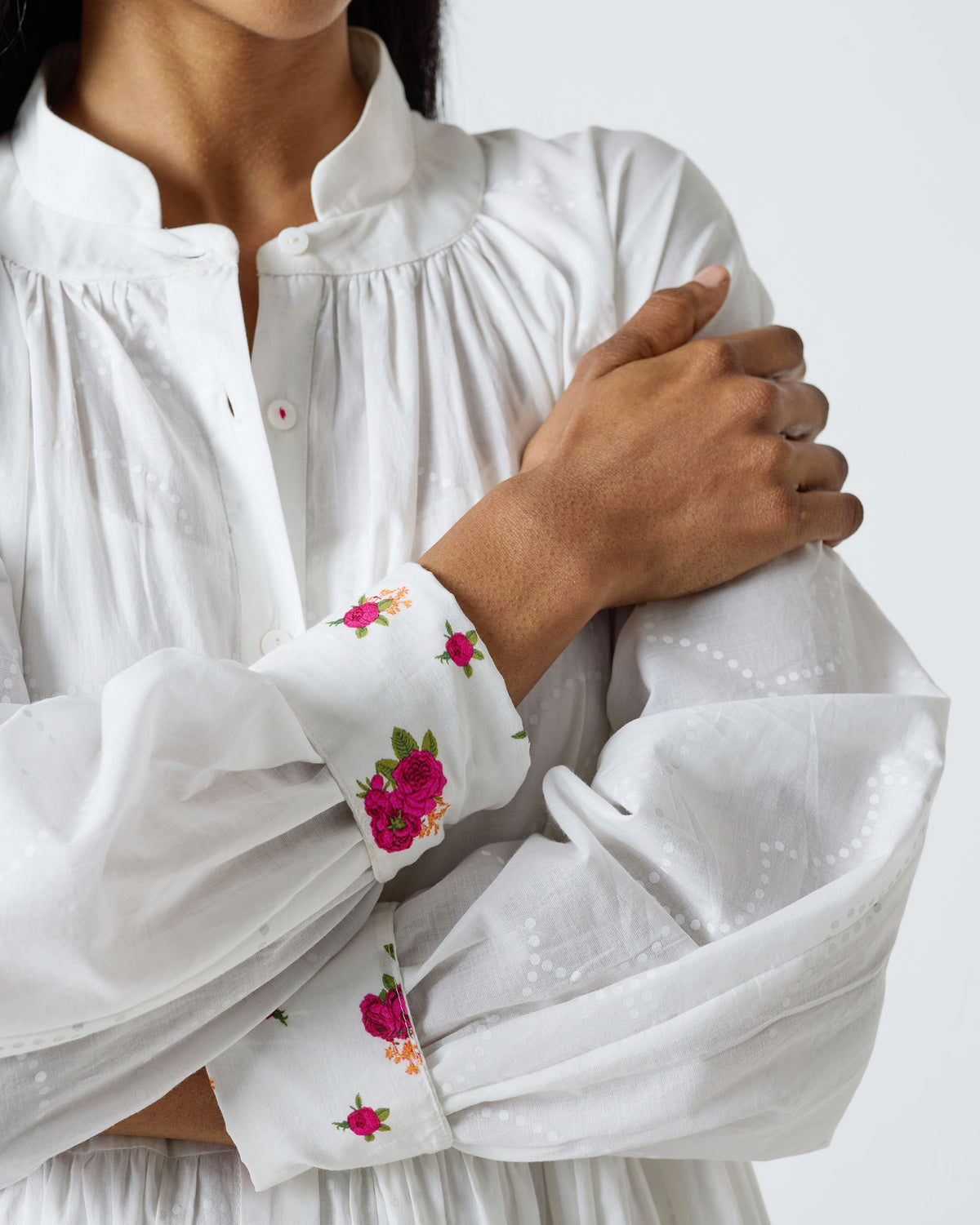 Close-up of pink rose embroidery on the cuffs of a white Miya dress.