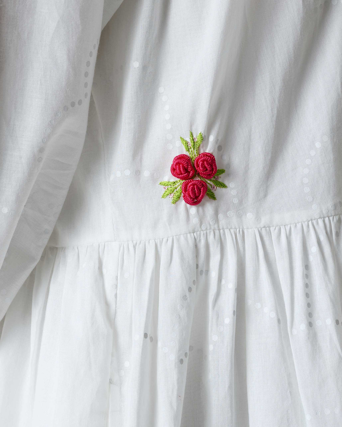 Close-up of pink rose embroidery at the waist of a white Miya dress.