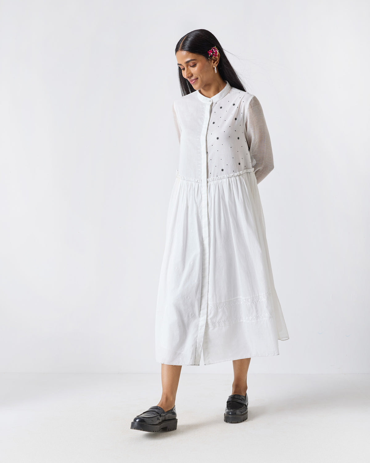 Person wearing a white Rayna dress with black embroidery accents and a flared midi skirt.