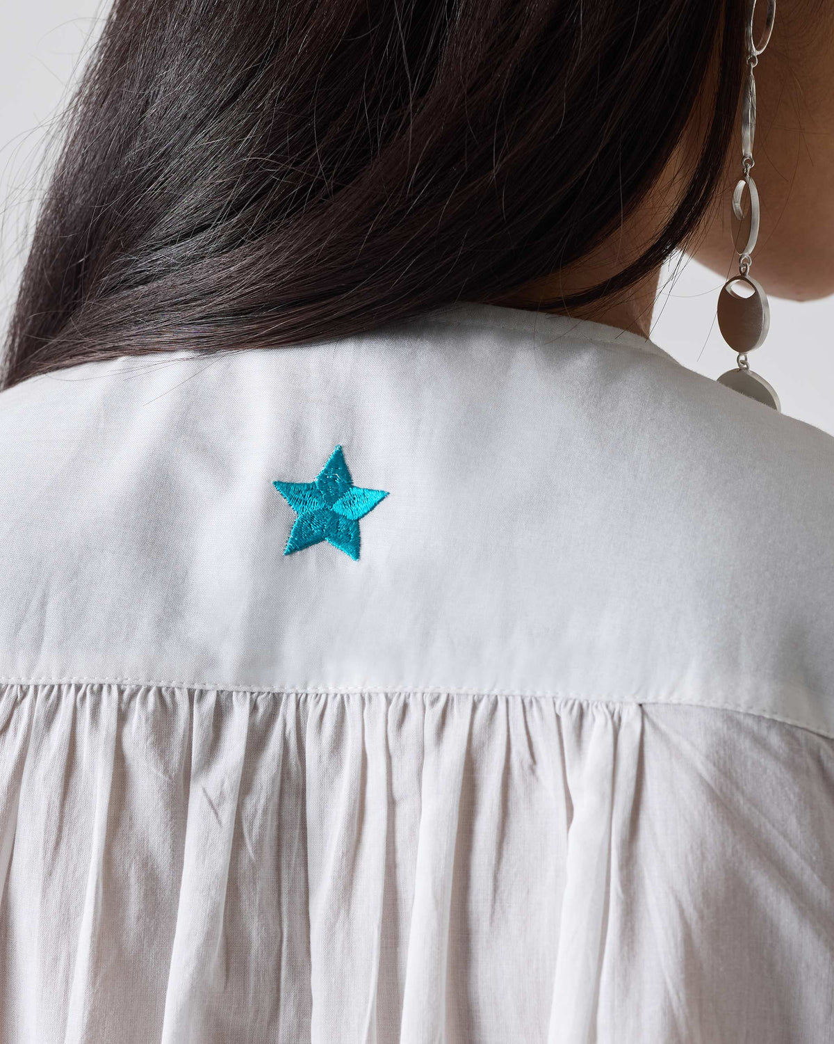 Close-up of a turquoise embroidered star on the back of a white Pleated Waist kurta.