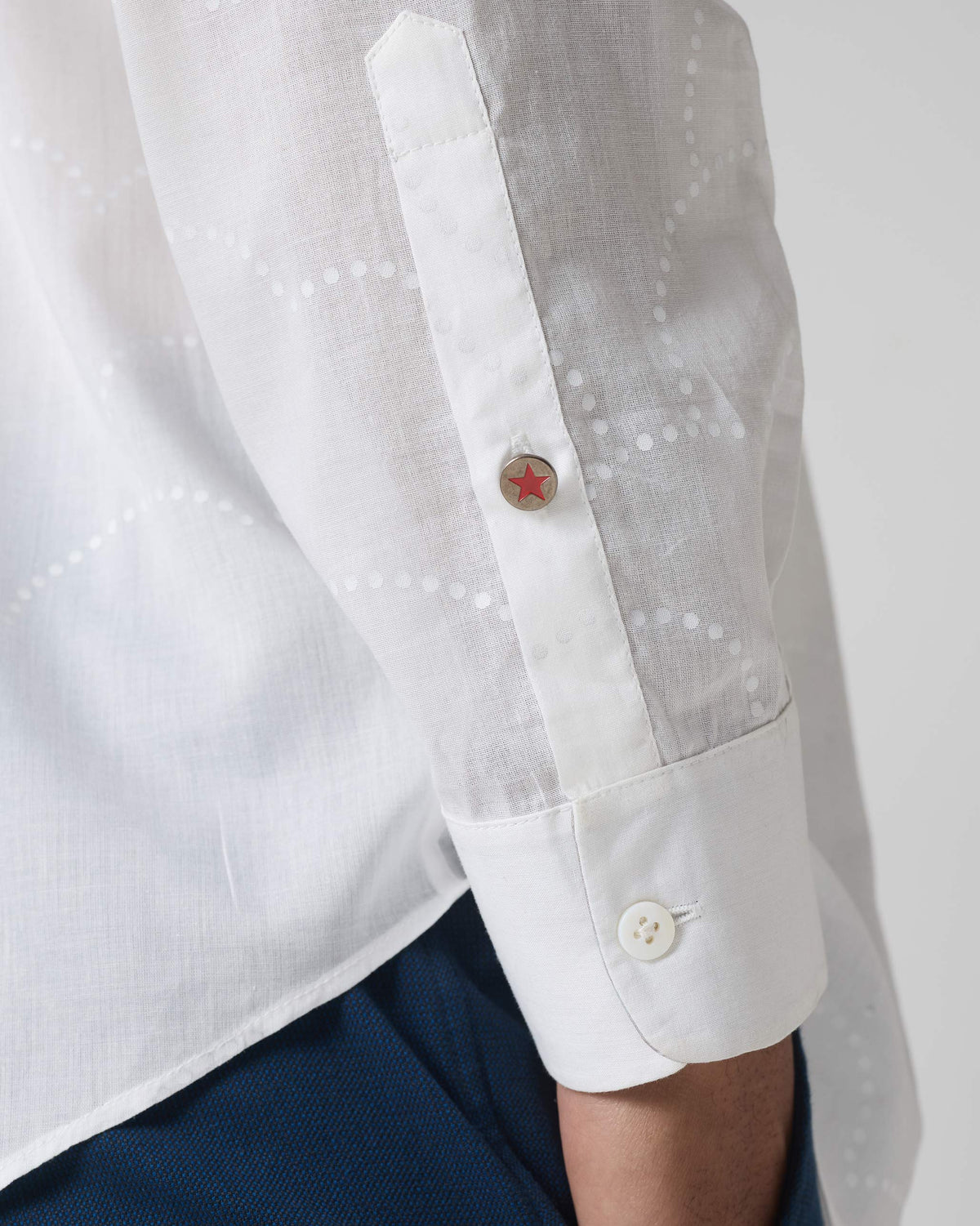 Close-up of a white Hakuna Shirt sleeve showing dotted wave embroidery and a red star button.