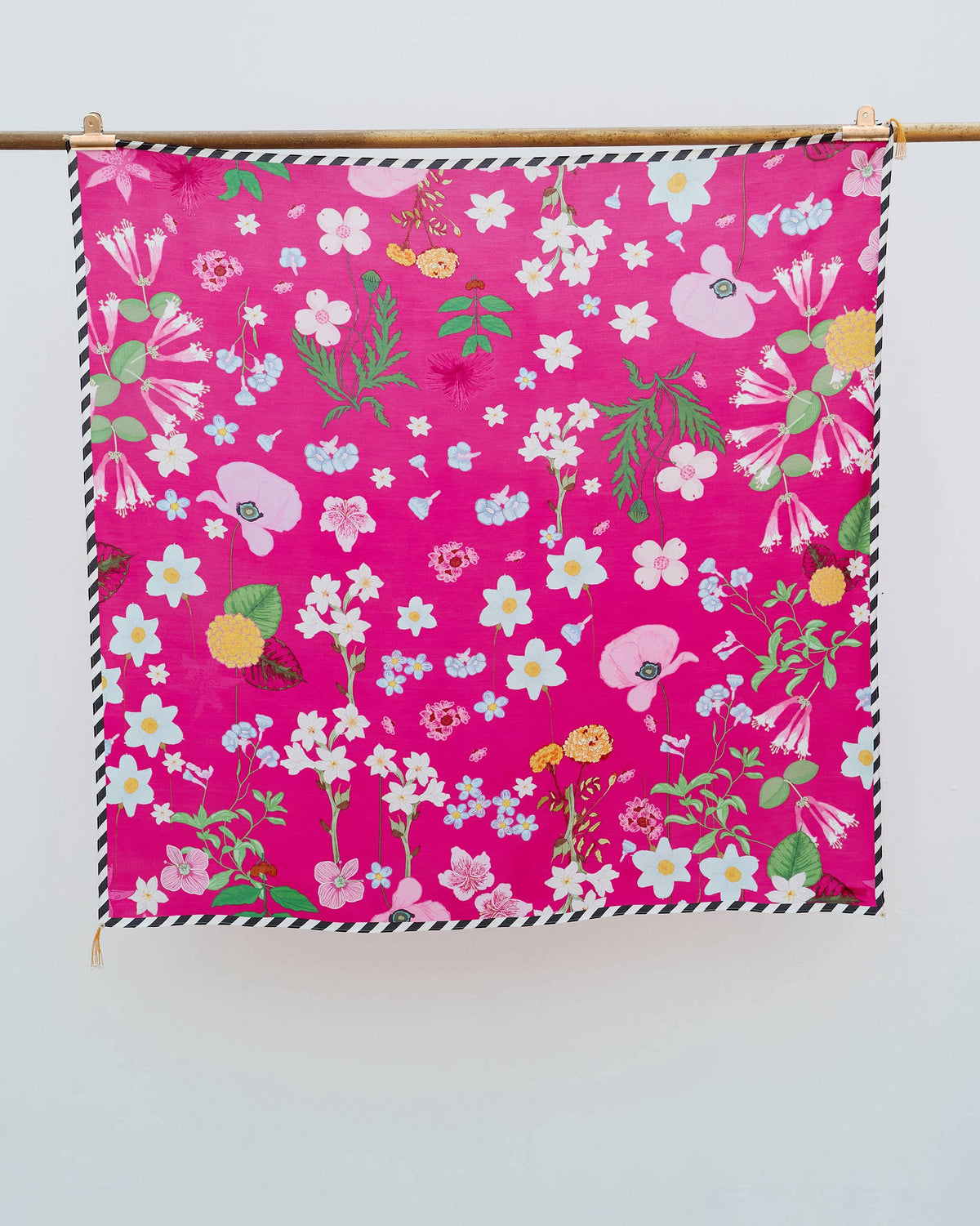 Wildflower Scarf hung from a rod, in fuchsia with white and blue flowers.