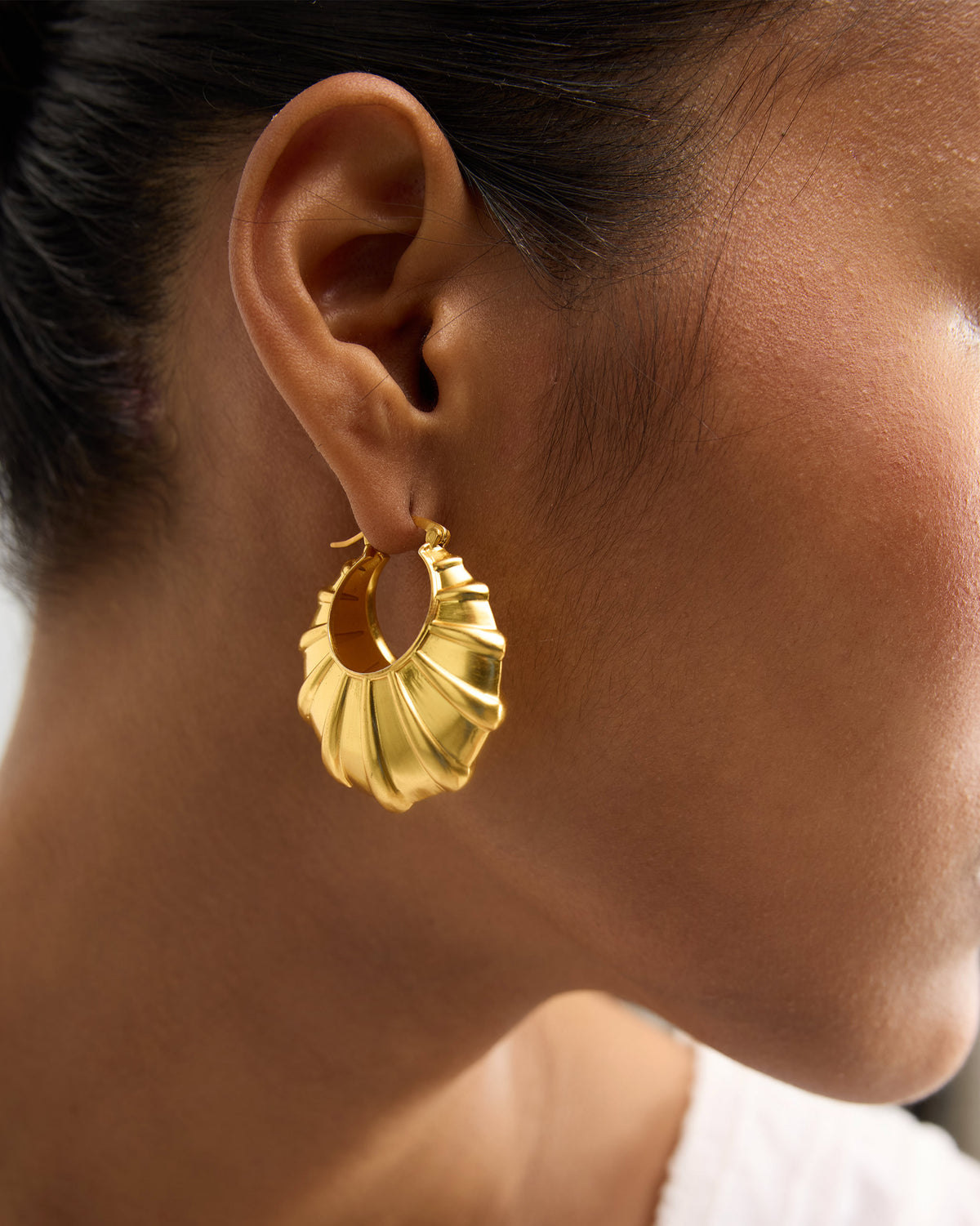 Close-up of gold Shell Balis worn on an ear, showing the ridged shell shape.