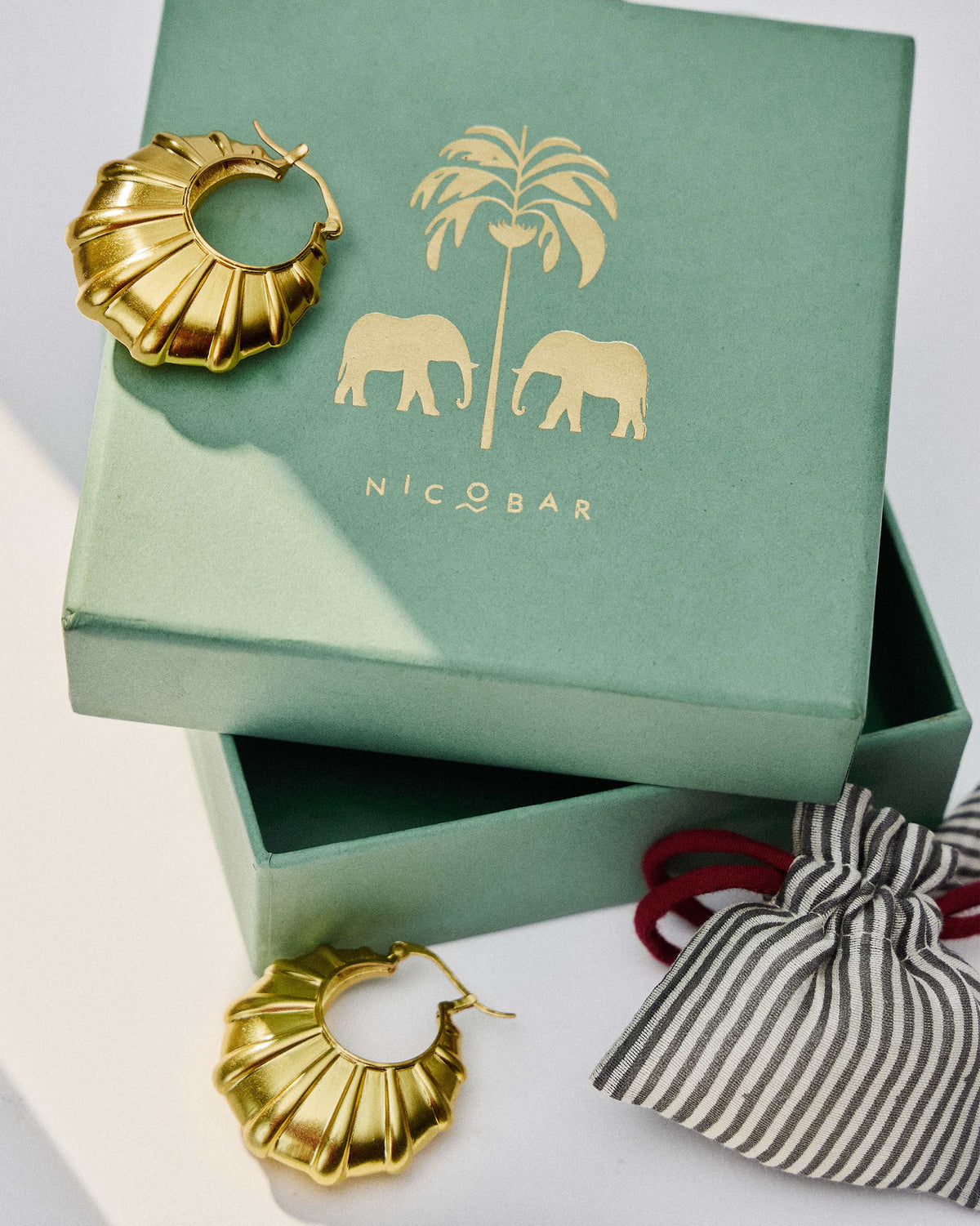 Pair of gold Shell Balis displayed on a green Nicobar gift box.