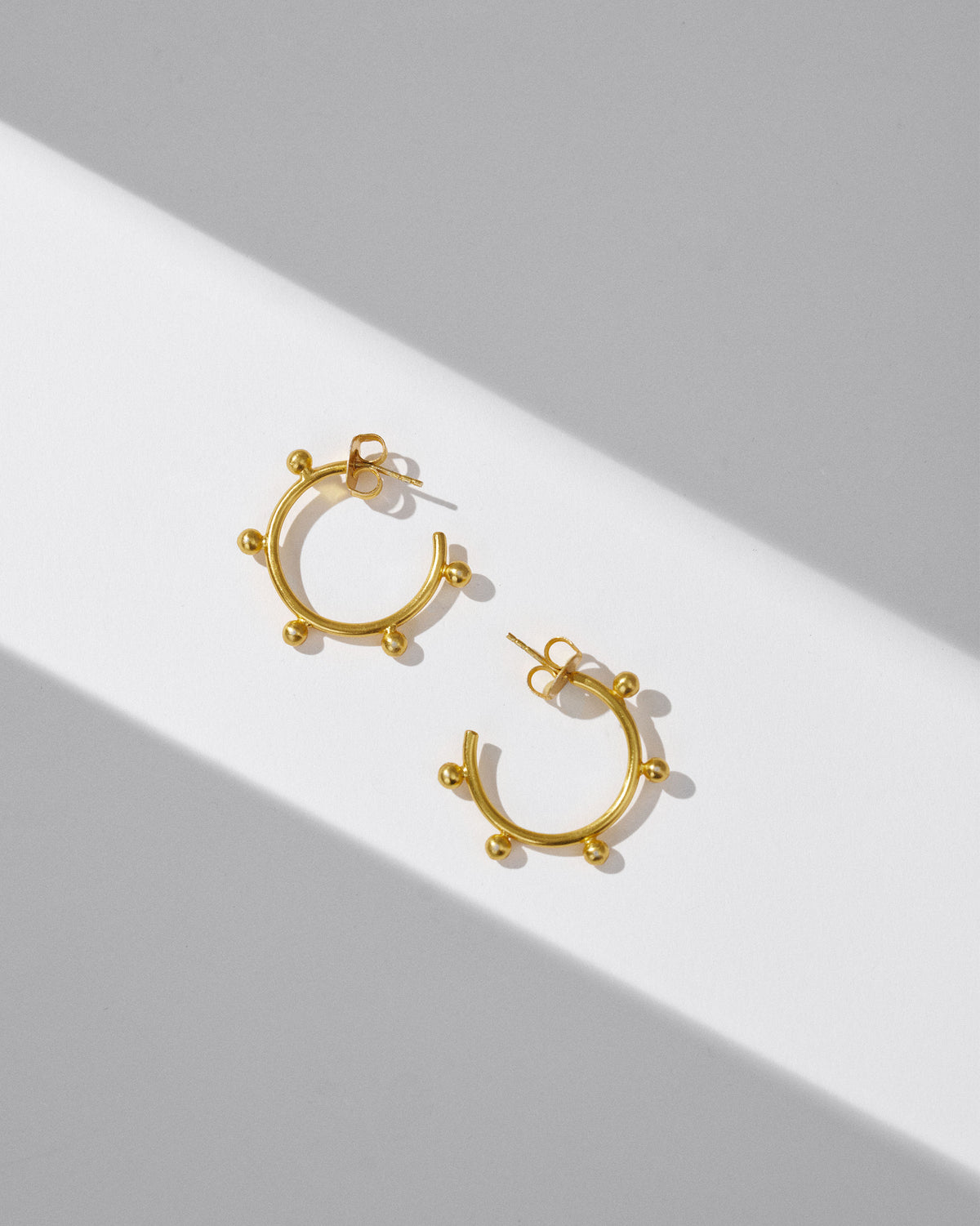 Pair of gold Sunshine hoops with outer beads laid flat.