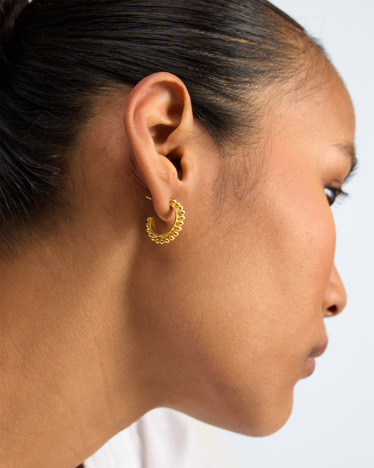 Side view of gold Rava Hoops Small worn on a person, showing beaded edges.
