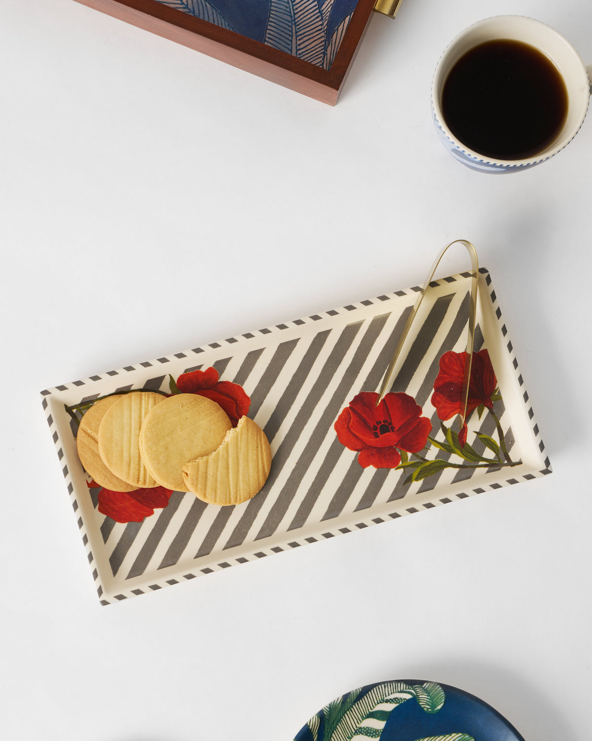 Striped Poppy cookie tray holding biscuits with gold tongs beside a coffee cup.