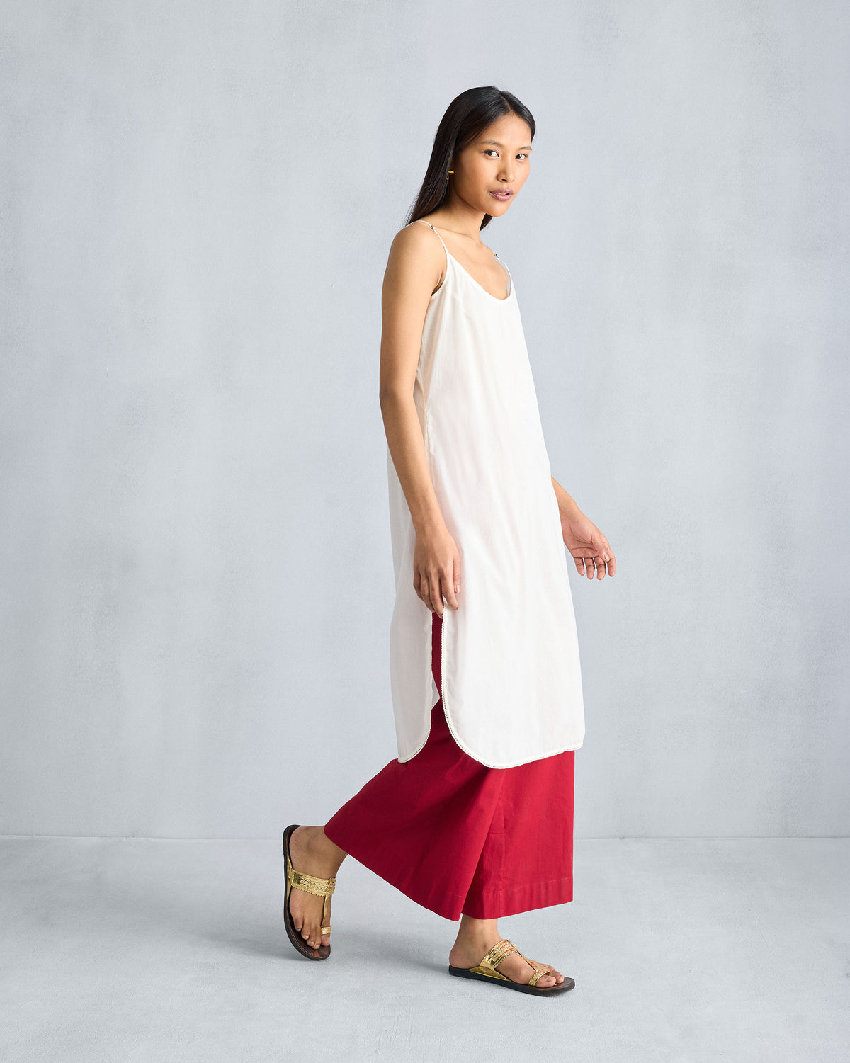 Side view of an ivory vintage camisole with side slits over red pants.
