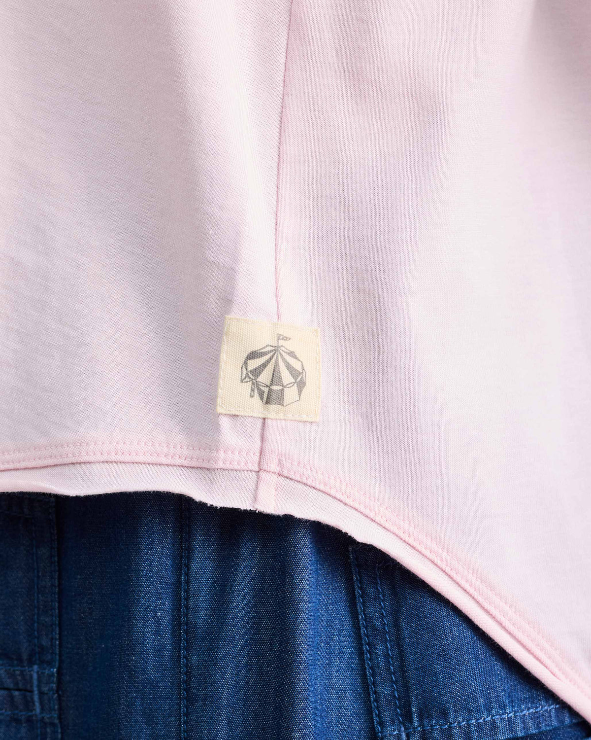 Close-up of a light pink Ukiyo tank hem with a small tent logo patch.