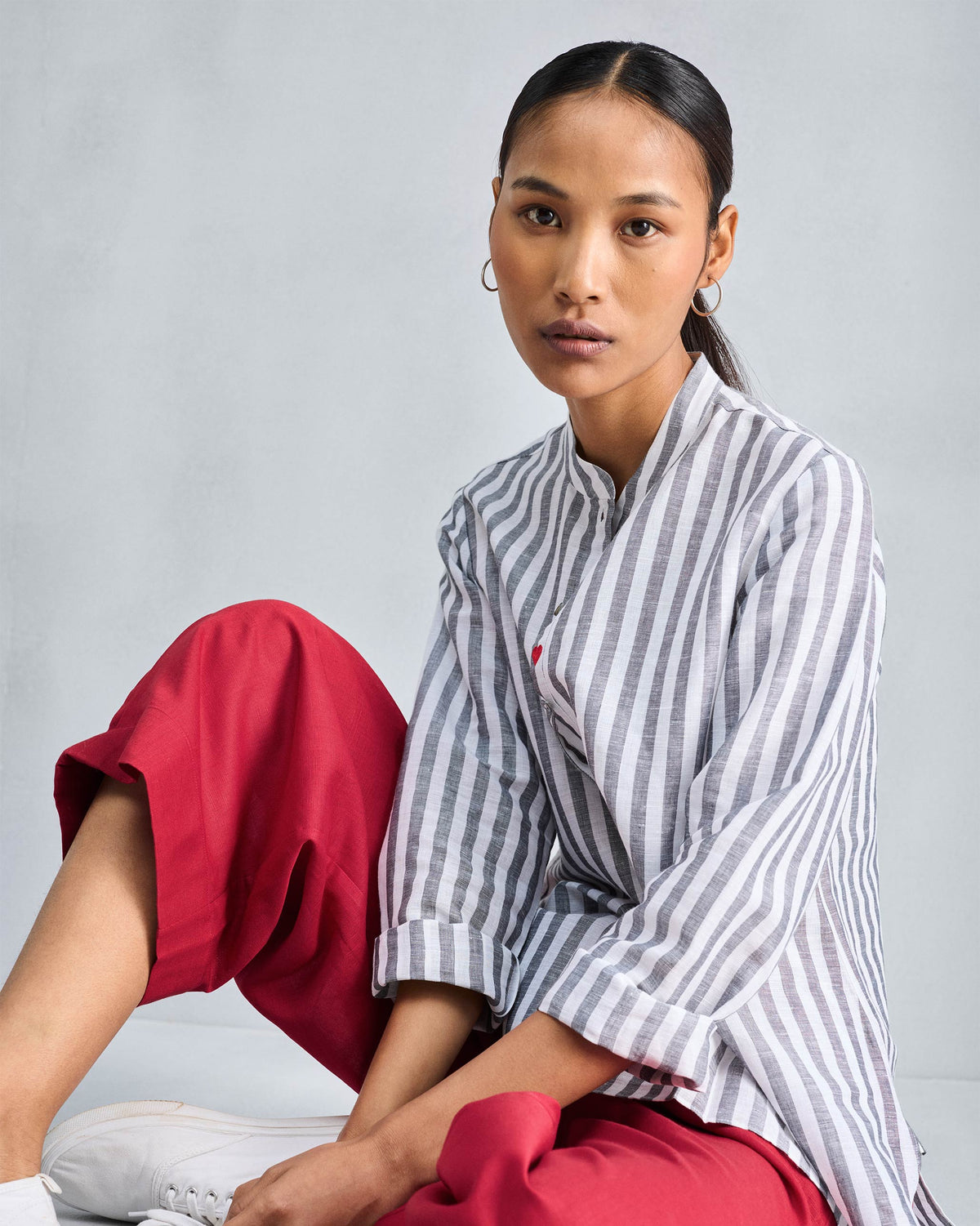 Person wearing a striped mandarin collar top with a red heart.
