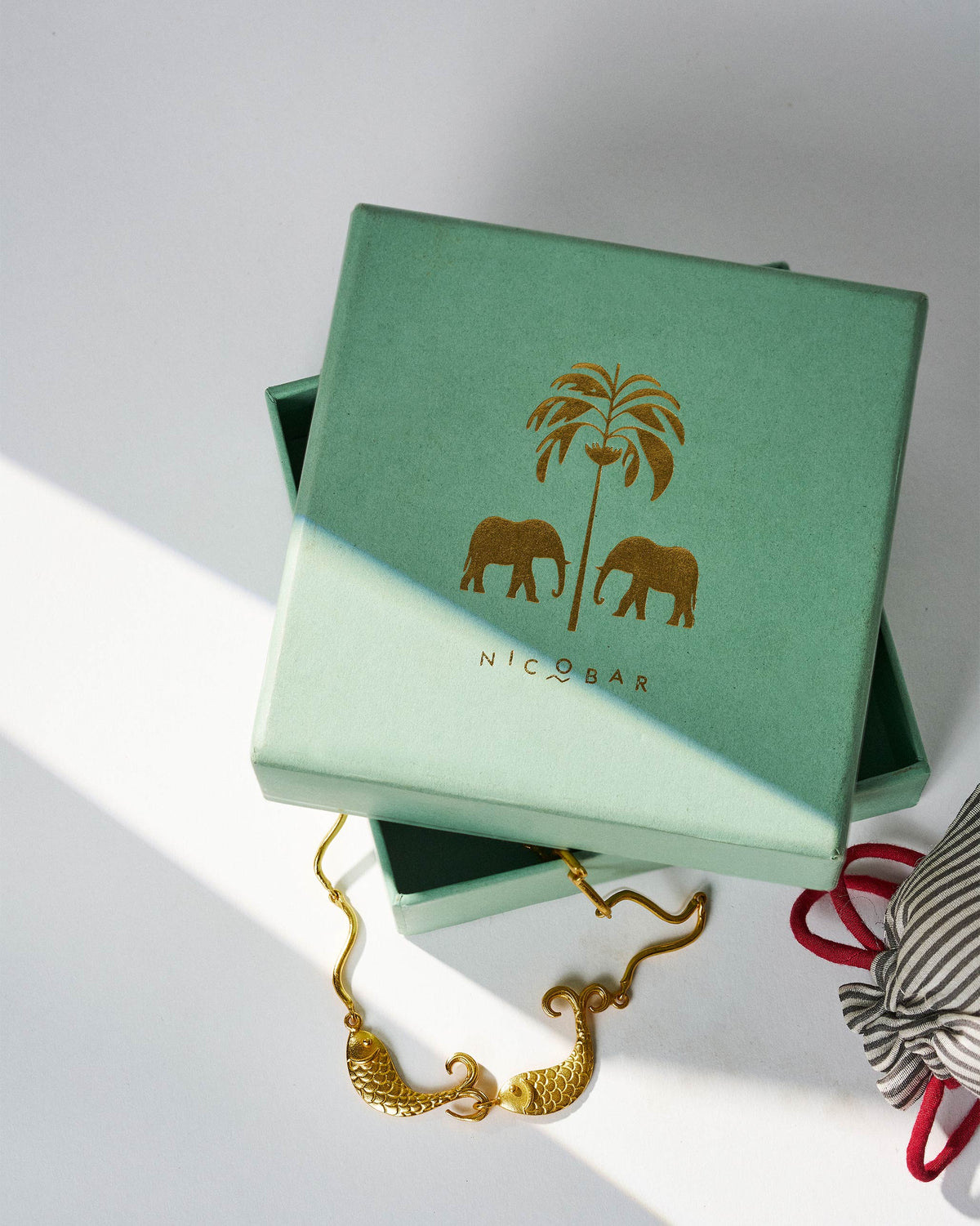 Gold Meen necklace with twin fish on a Nicobar gift box.