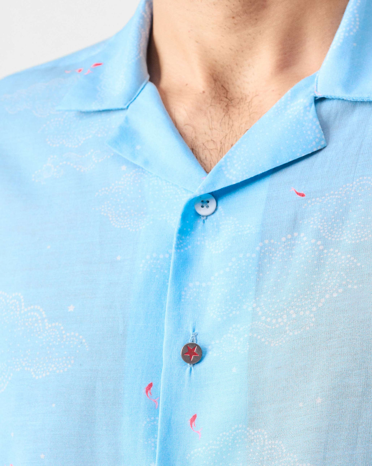 Close-up of a light blue Mistari Shirt showing cloud print and a red star button.