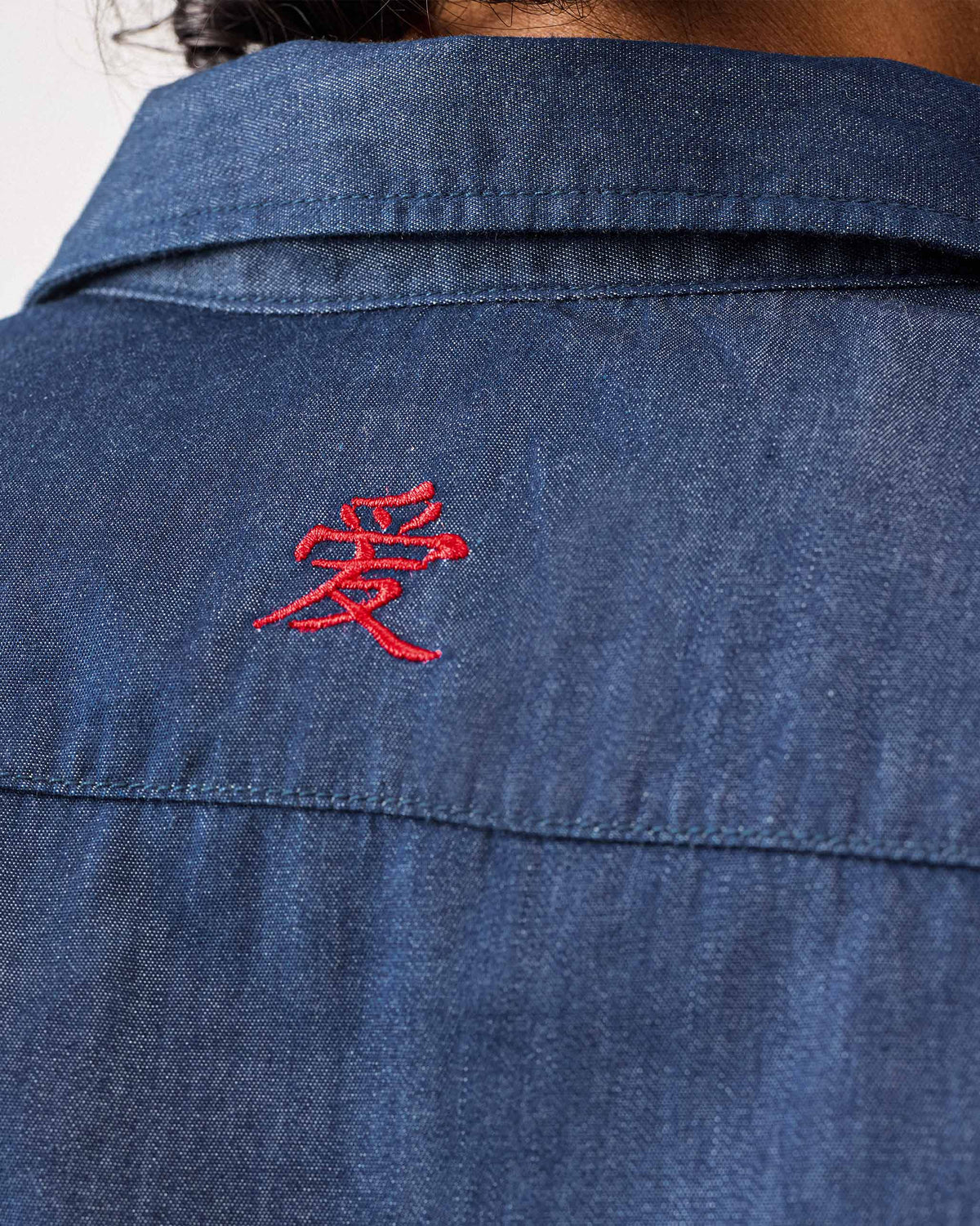 Close-up of the red embroidered love character on the back of a denim Konbini Shirt.