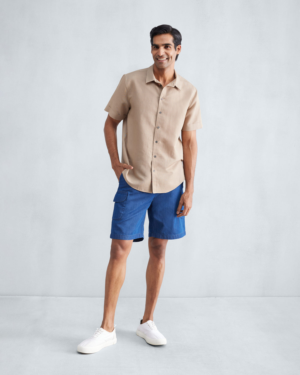 Person wearing a beige half-sleeve shirt untucked over blue shorts.