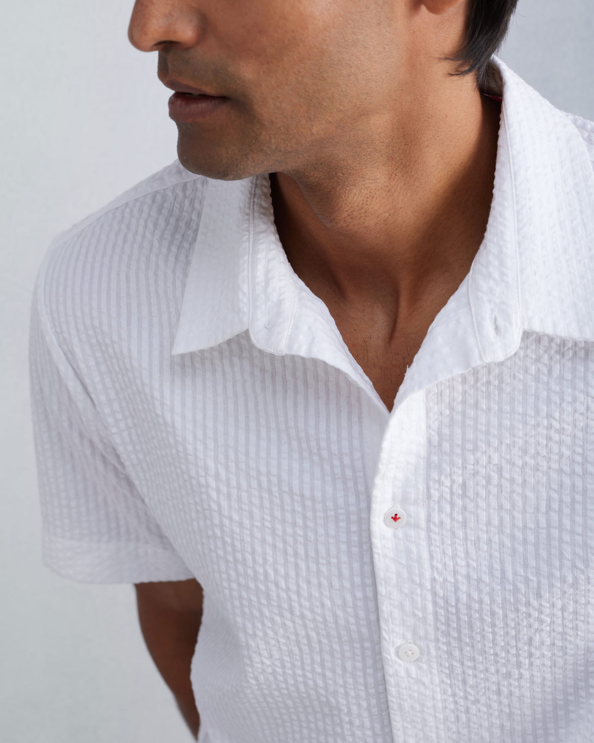 Close-up of a white seersucker shirt with red stitching on a button.
