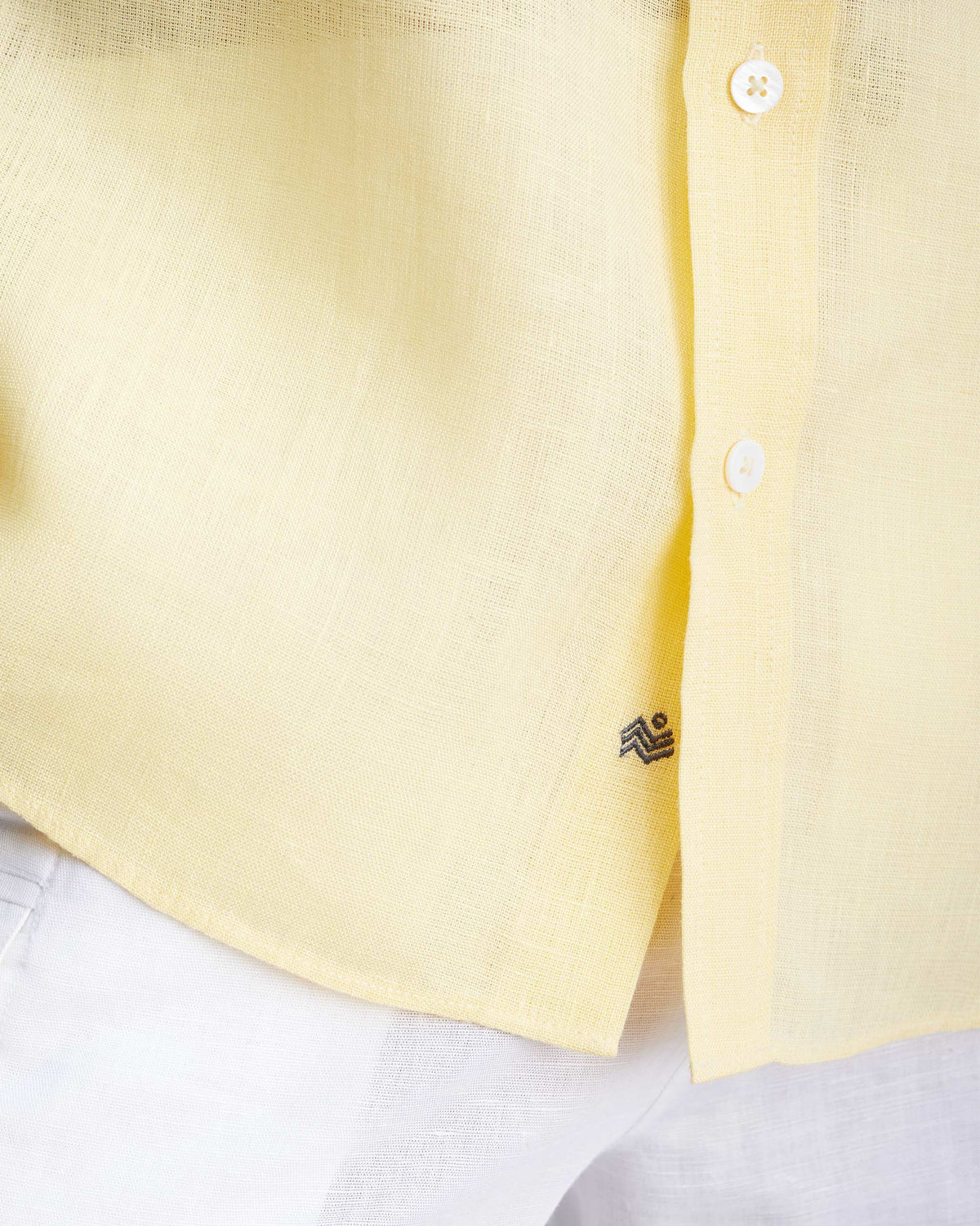 Close-up of a lemon shirt hem with white buttons and a small wave embroidery.