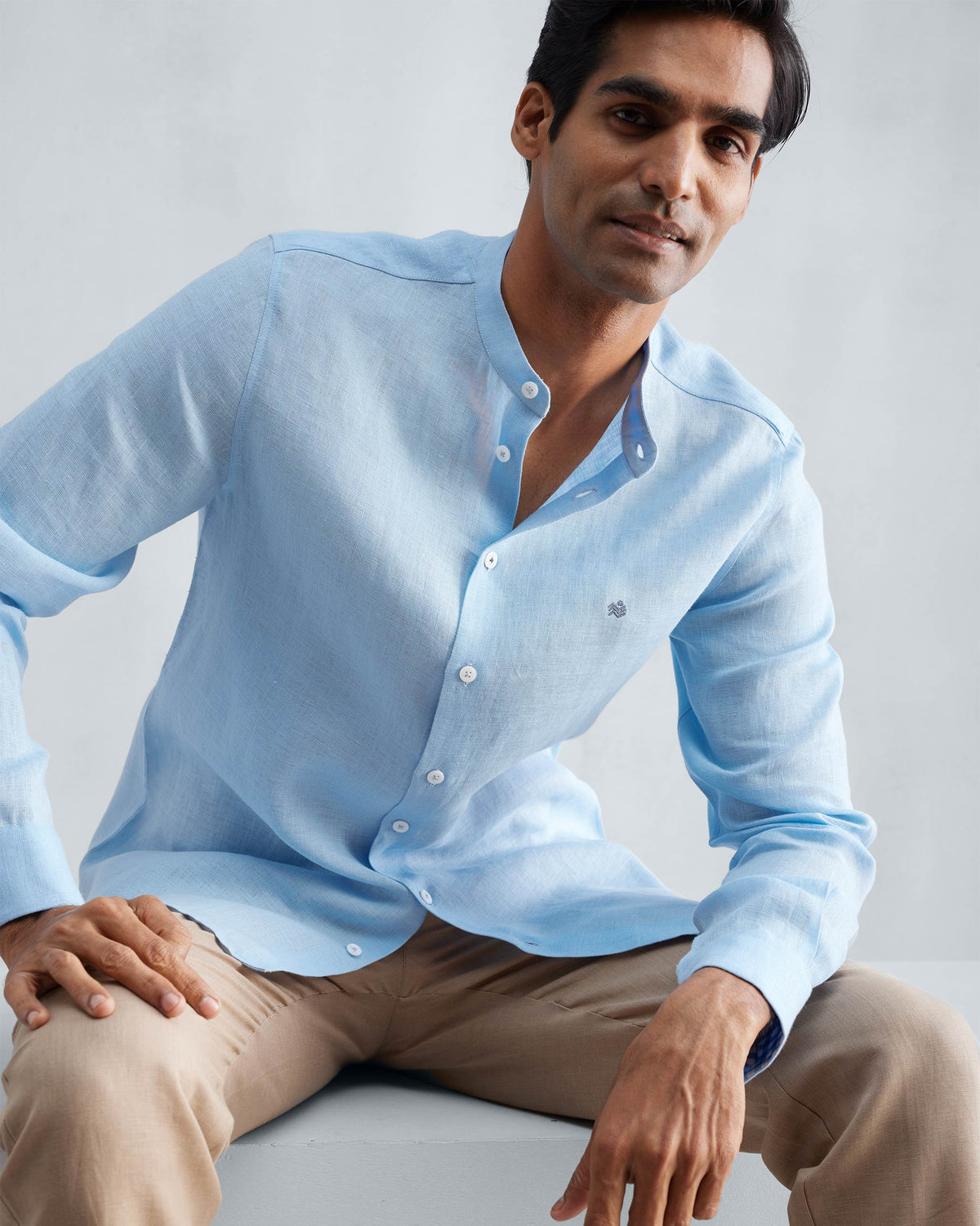 Person wearing a light blue Nehru collar Nawab shirt with a chest logomark.