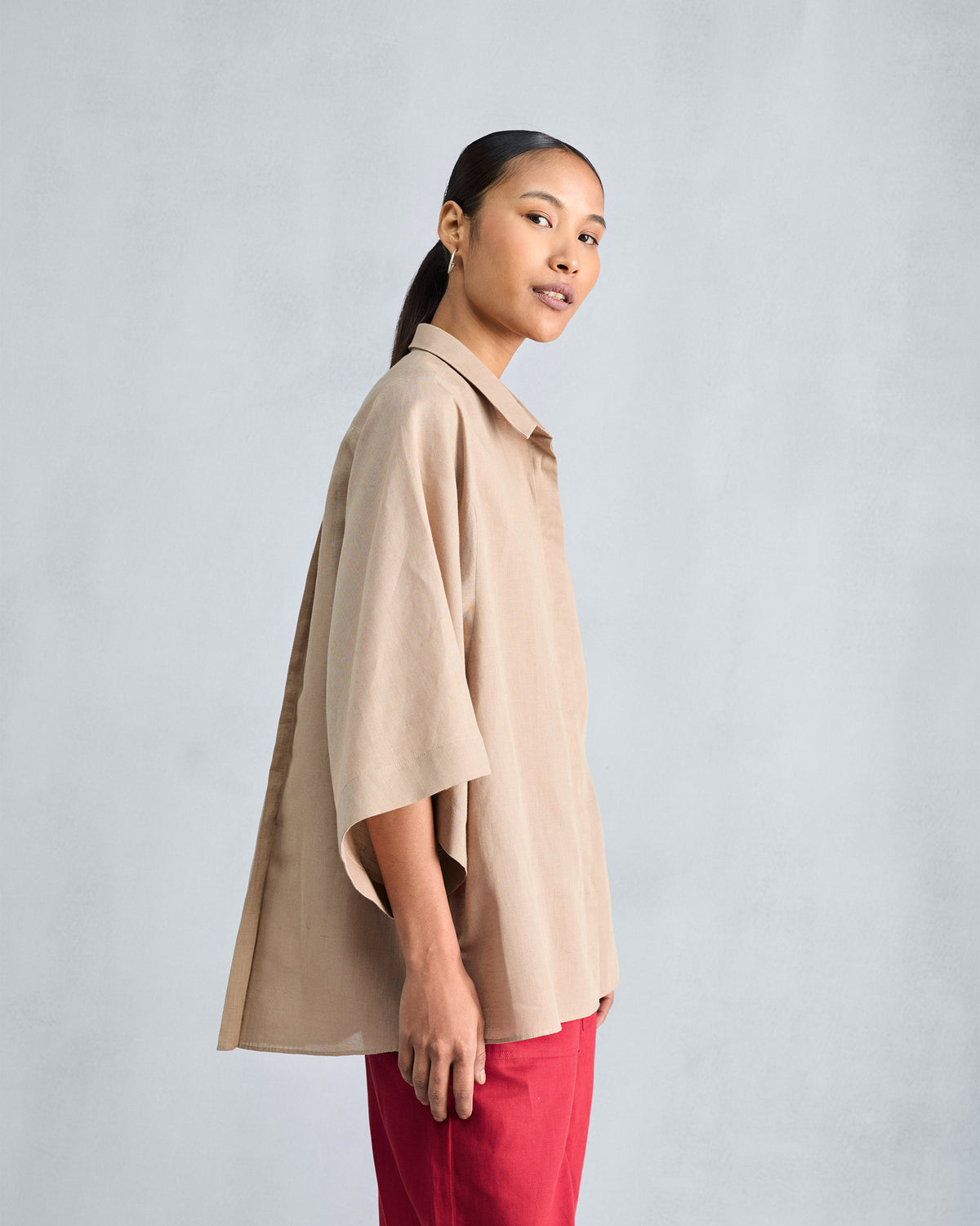 Side view of a beige drop armhole shirt showing its flared silhouette.