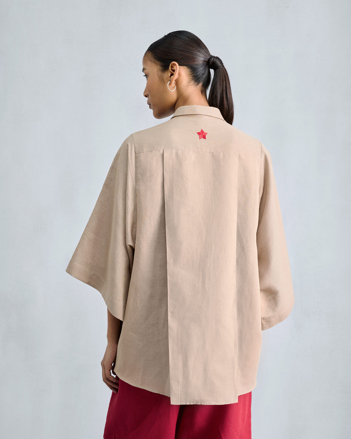 Back of a beige drop armhole shirt with a red embroidered star on the yoke.