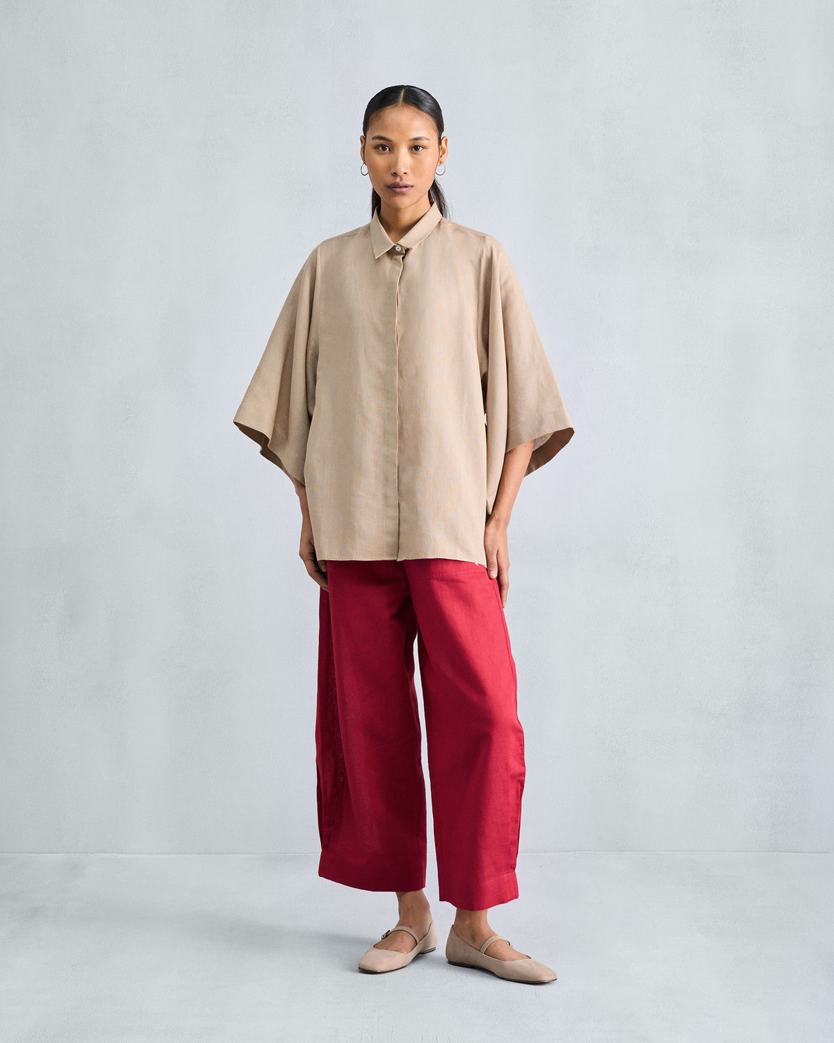 Full-length beige drop armhole shirt with wide sleeves over red trousers.