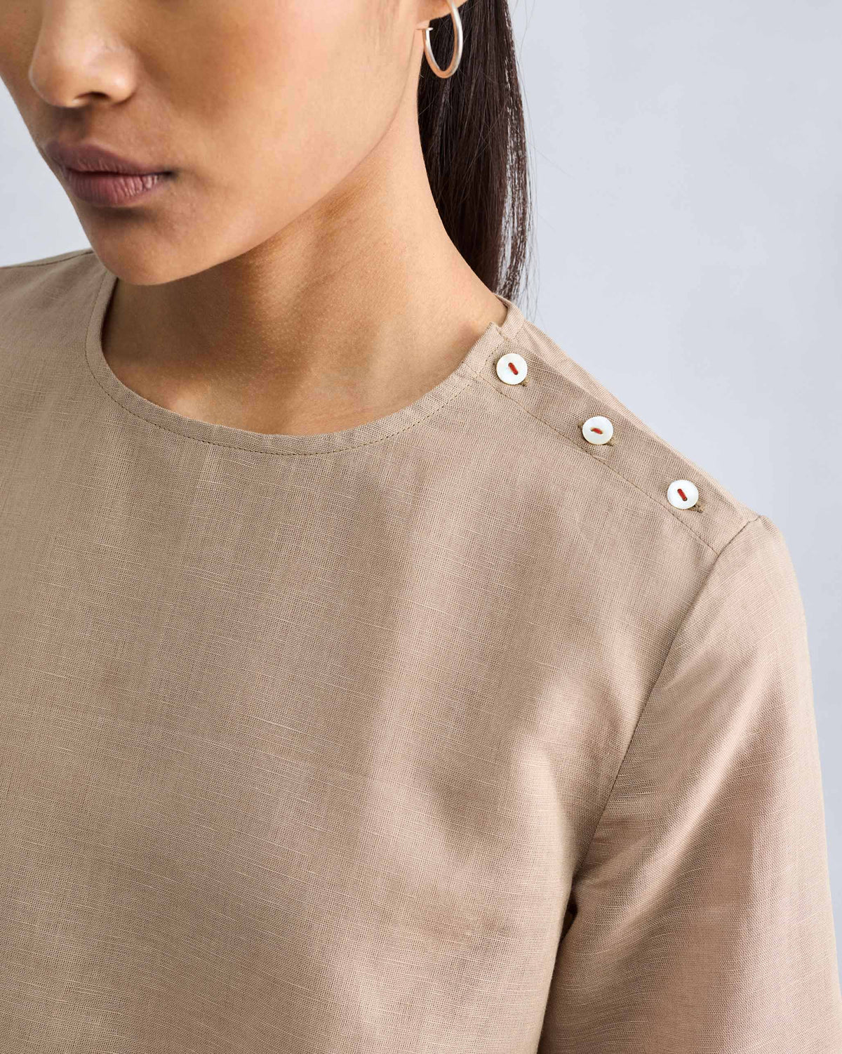 Close-up of a beige High Slit Top showing shoulder buttons with red stitching.