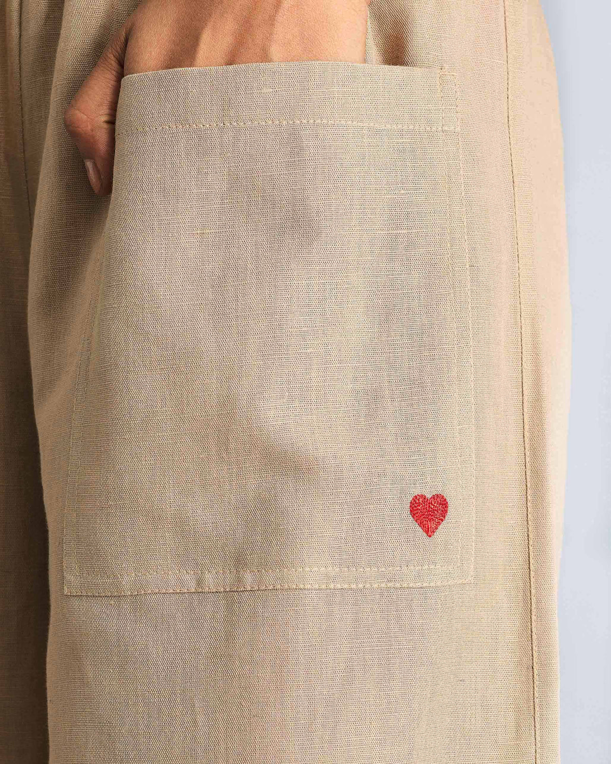 Close-up of beige serene pants showing a patch pocket and red heart.