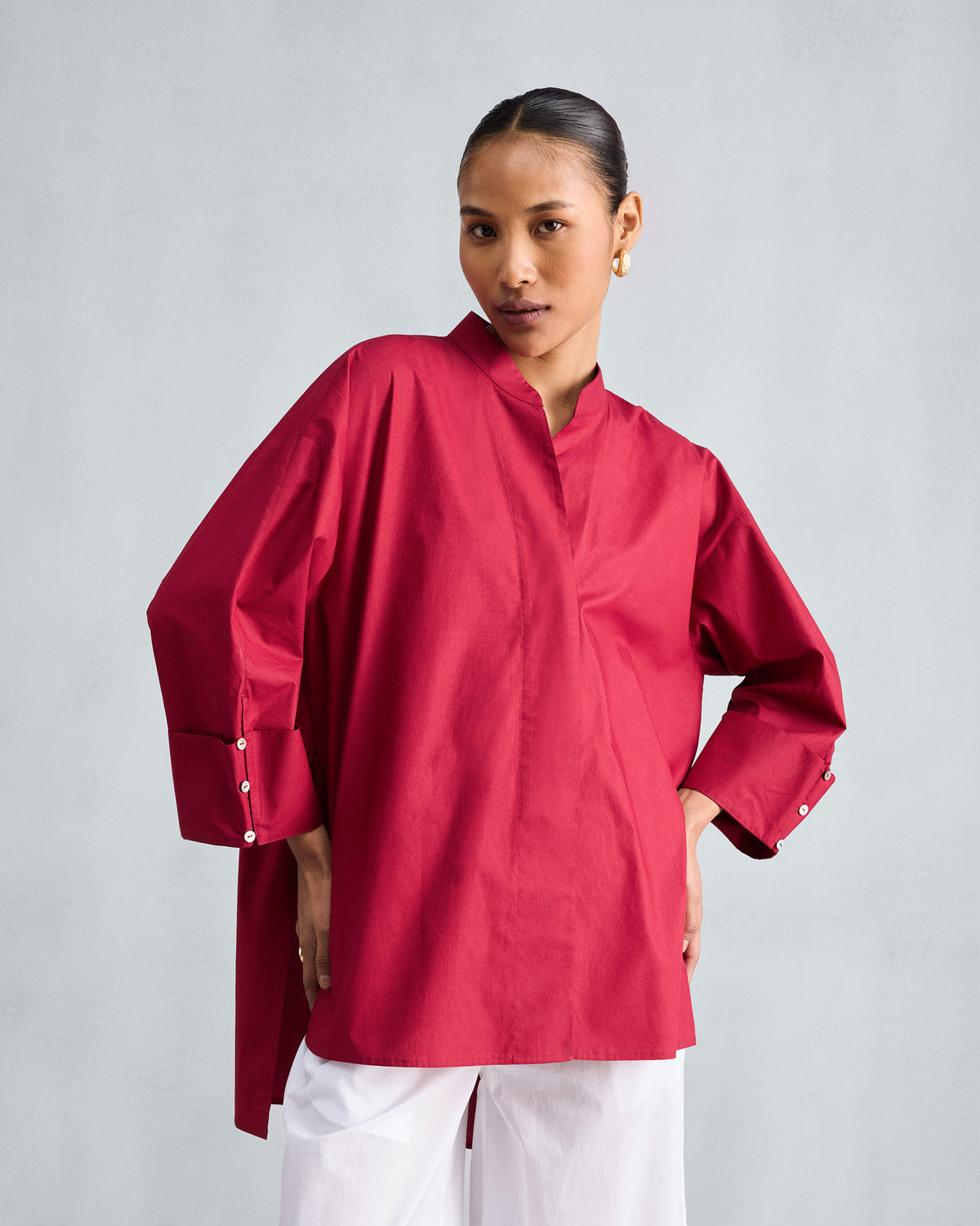 Person wearing a red Cirrus shirt with a band collar, wide buttoned cuffs, and a high-low hem.