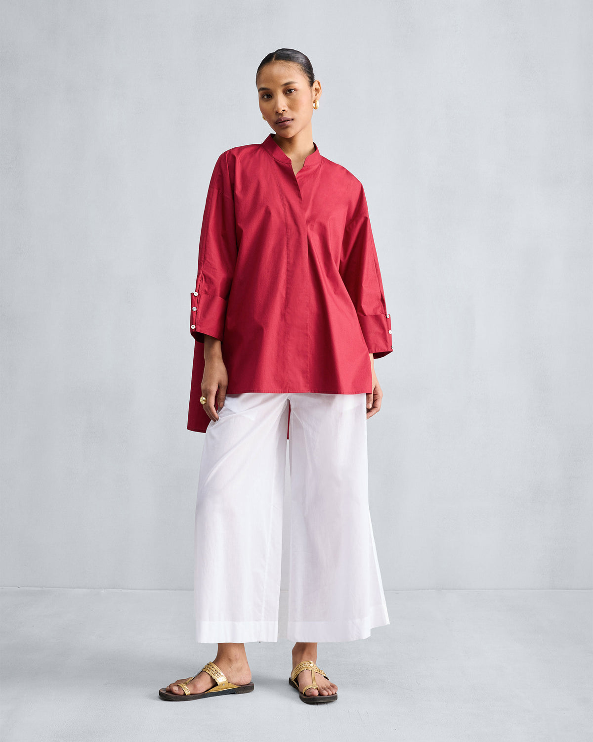 Person wearing a red Cirrus shirt with a high-low hem and wide buttoned cuffs.