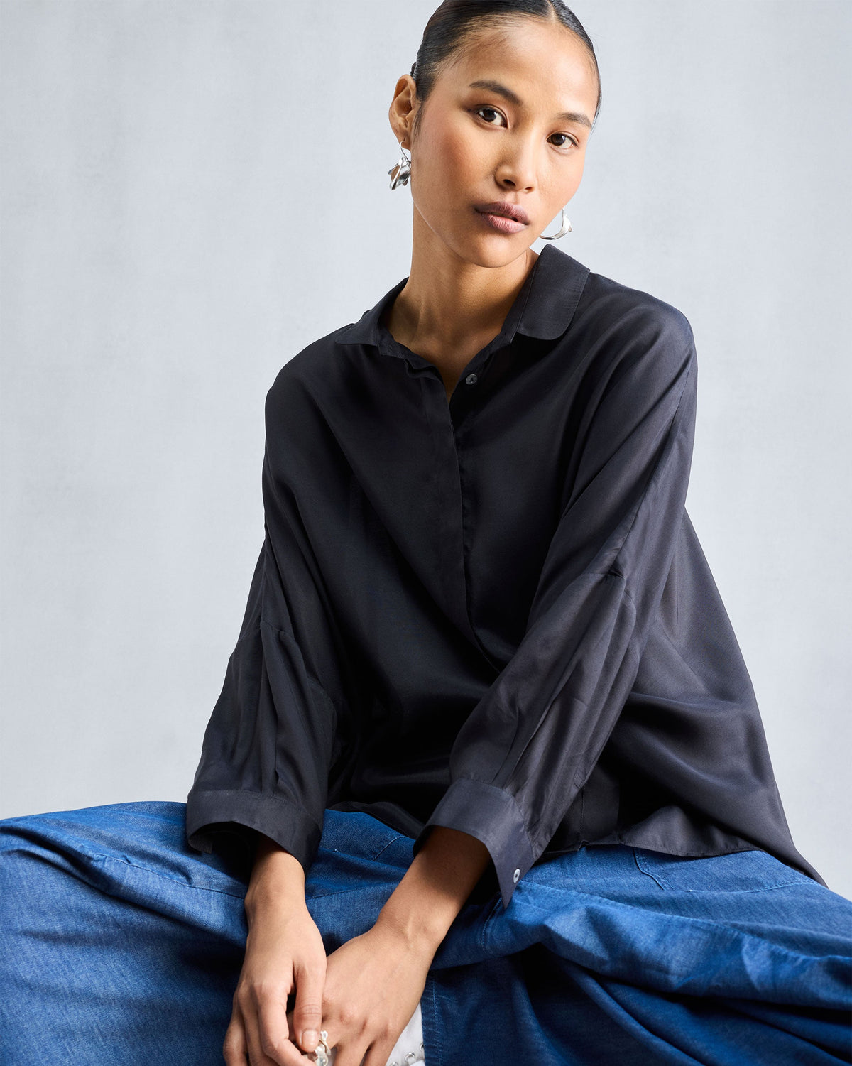 Person wearing a black boxy shirt with a pointed collar and wide cuffed sleeves.