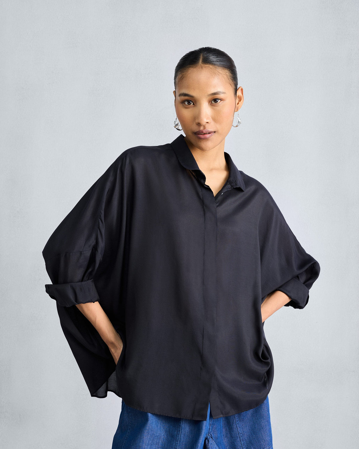 Person wearing a black boxy shirt with side pockets and rolled sleeves.