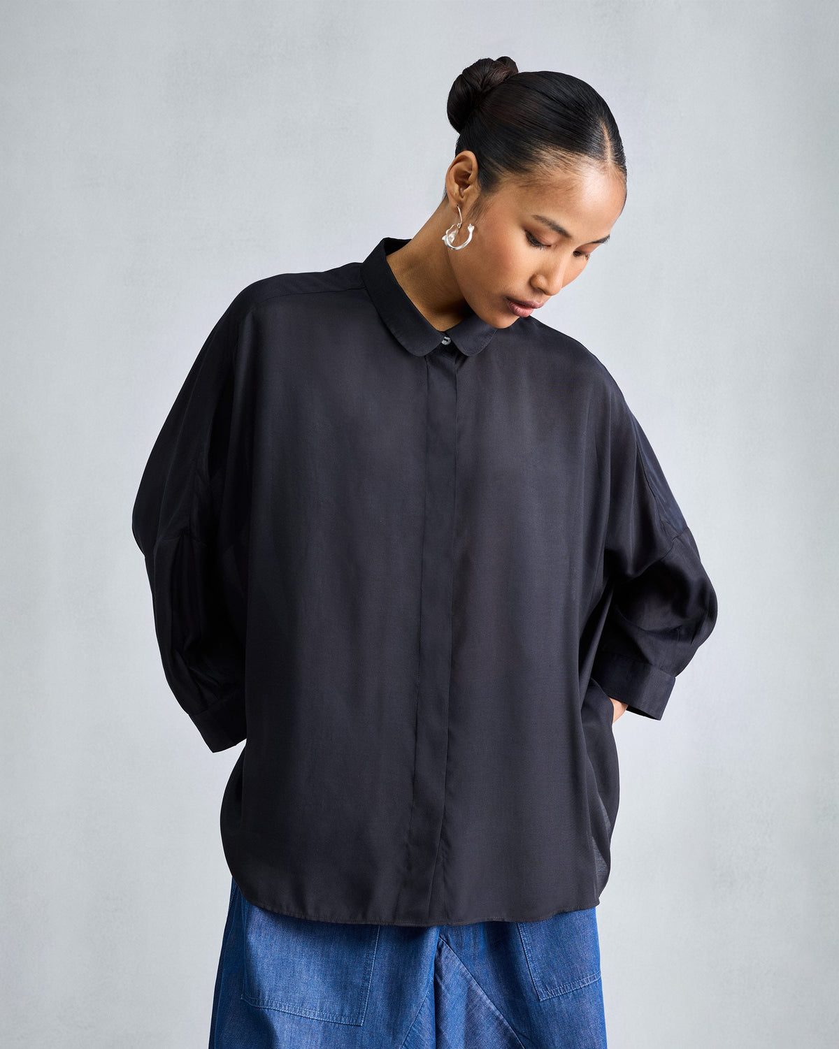Person wearing a black boxy shirt with a concealed placket and hip-length hem.