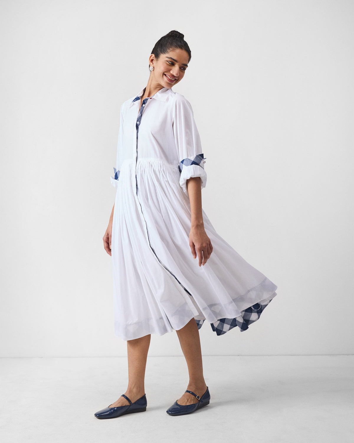 Person wearing a white Puritsu shirt dress with a pleated skirt and gingham accents.