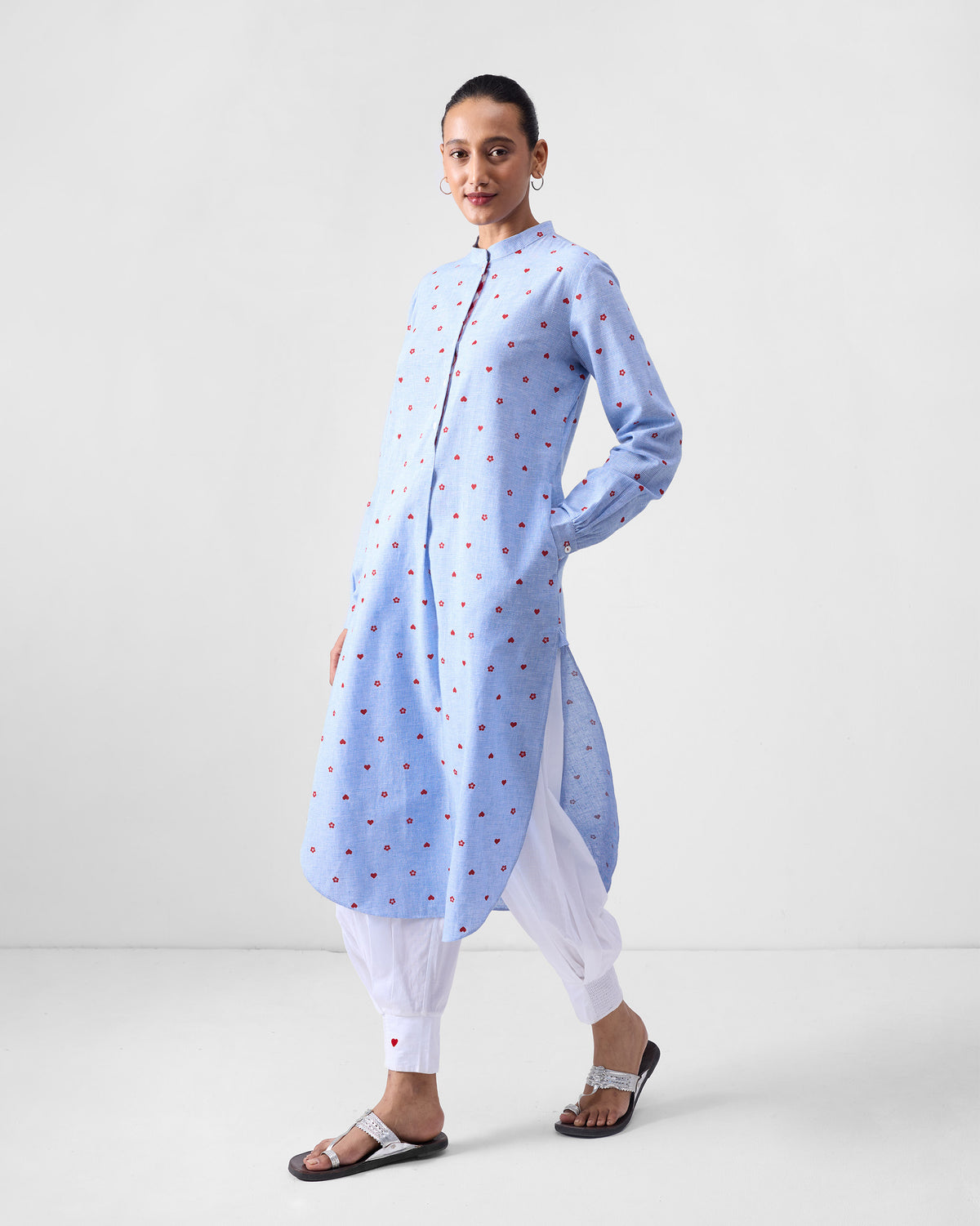 Person wearing a blue kurta with red heart and blossom motifs and a side pocket.