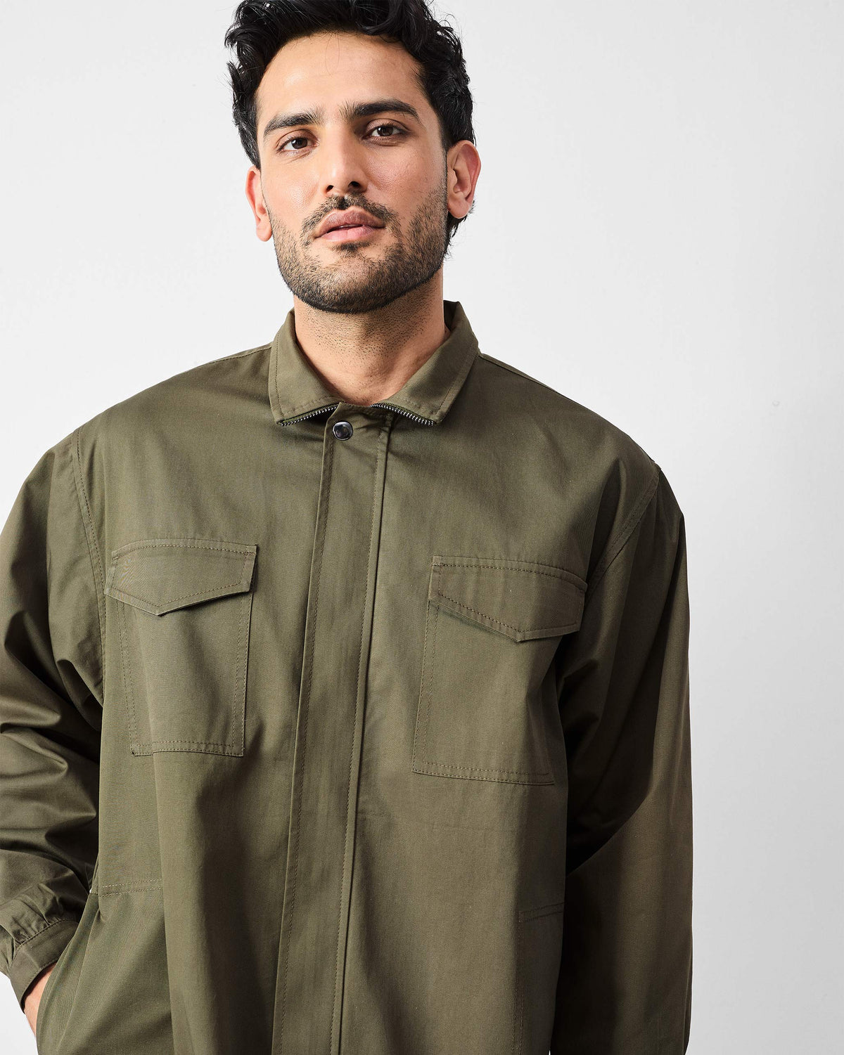 Person wearing an olive utility jacket with a pointed collar and chest pockets.