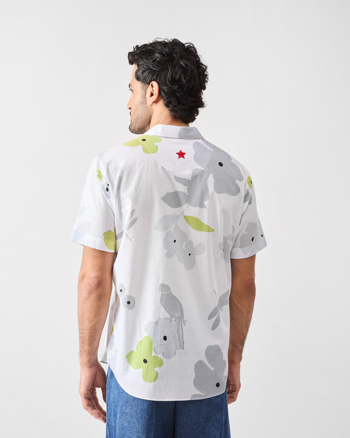 Back of a white Mistari Shirt with a parrot floral print and a red embroidered star.