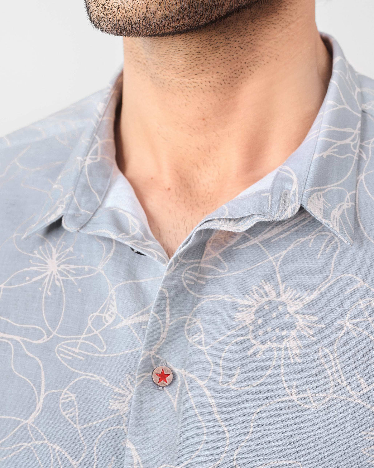 Close-up of a grey Riverline shirt collar with a red star button.