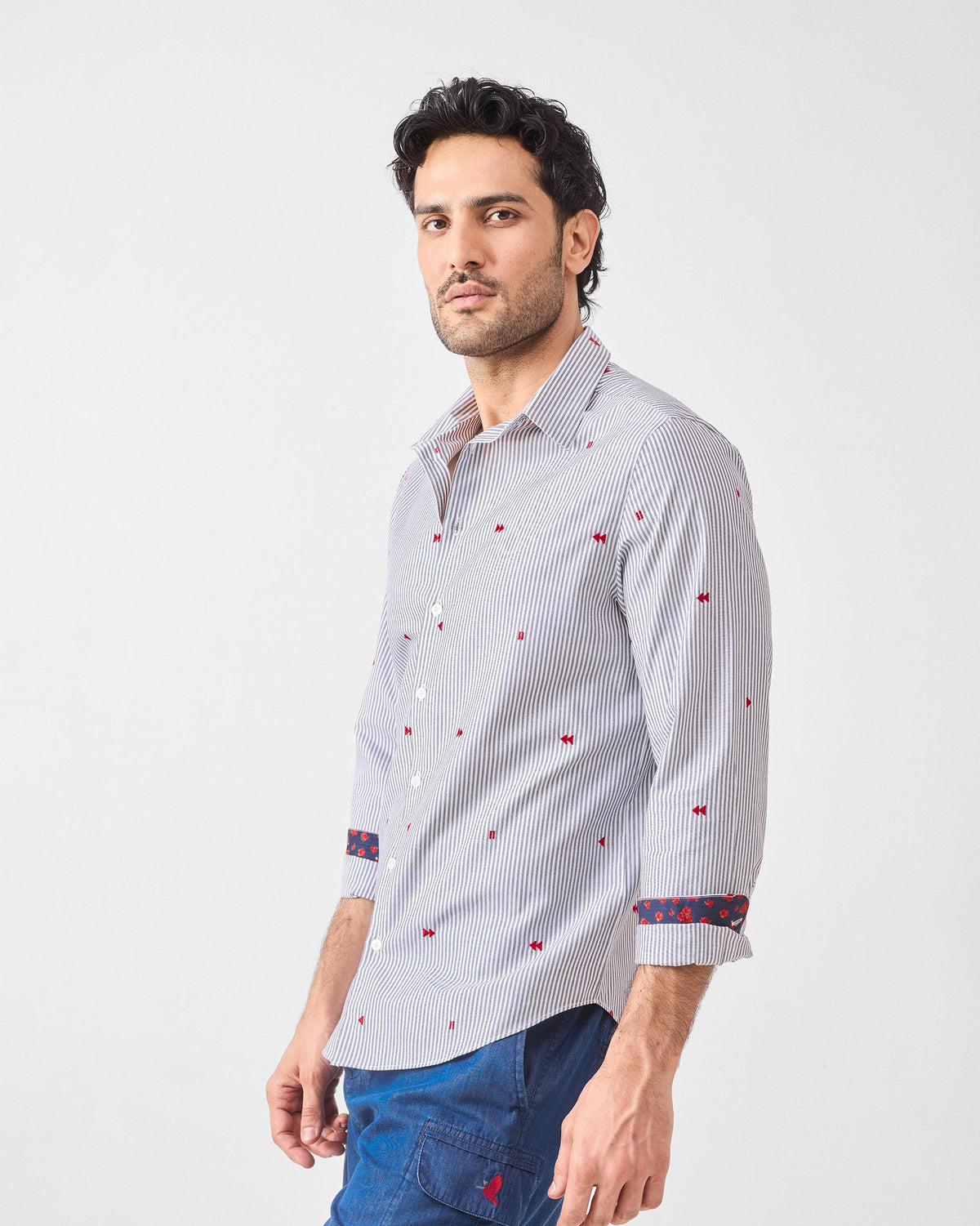 Three-quarter view of a white pinstripe Hakuna Shirt with red embroidery.