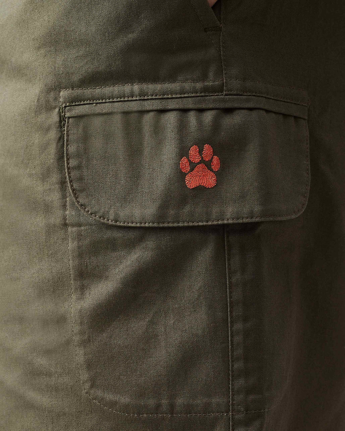 Close-up of an olive utility shorts cargo pocket with a paw embroidery.