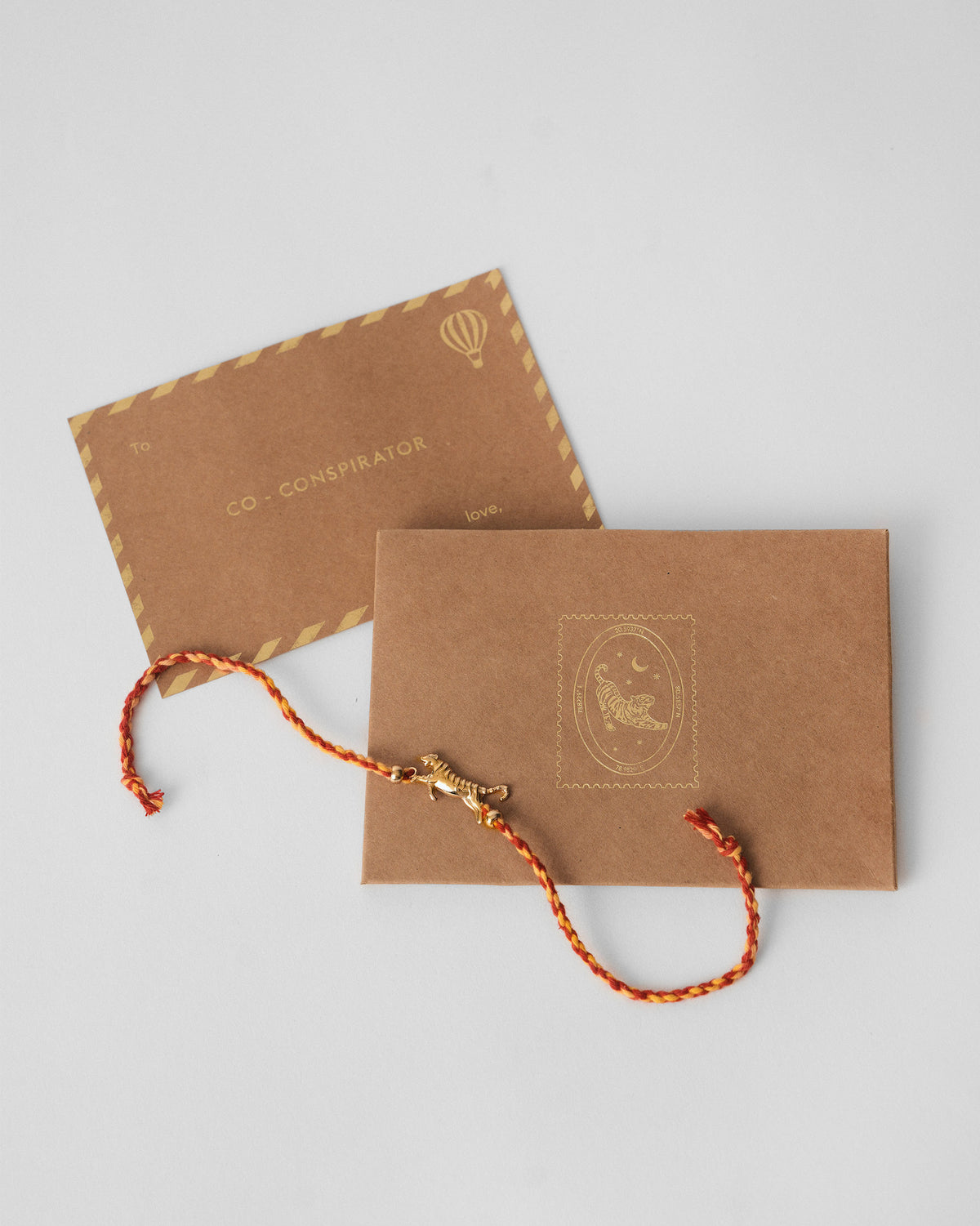 Tiger Rakhi in red with a gold tiger charm laid over a kraft envelope.