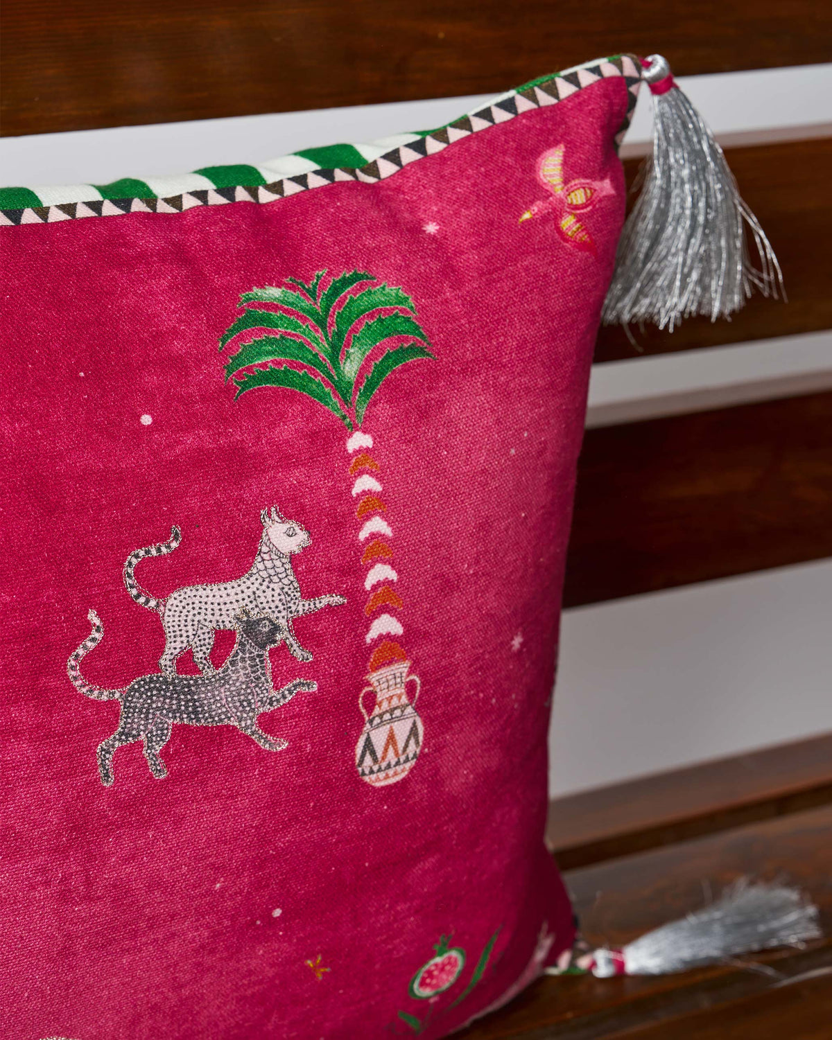 Close-up of a Harappa cushion cover with stacked leopards beside a patterned palm.