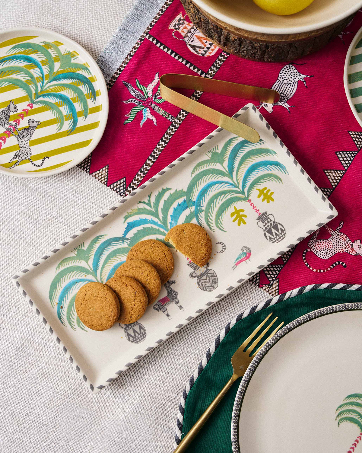 Indus cookie tray holding cookies with gold tongs on a patterned table.