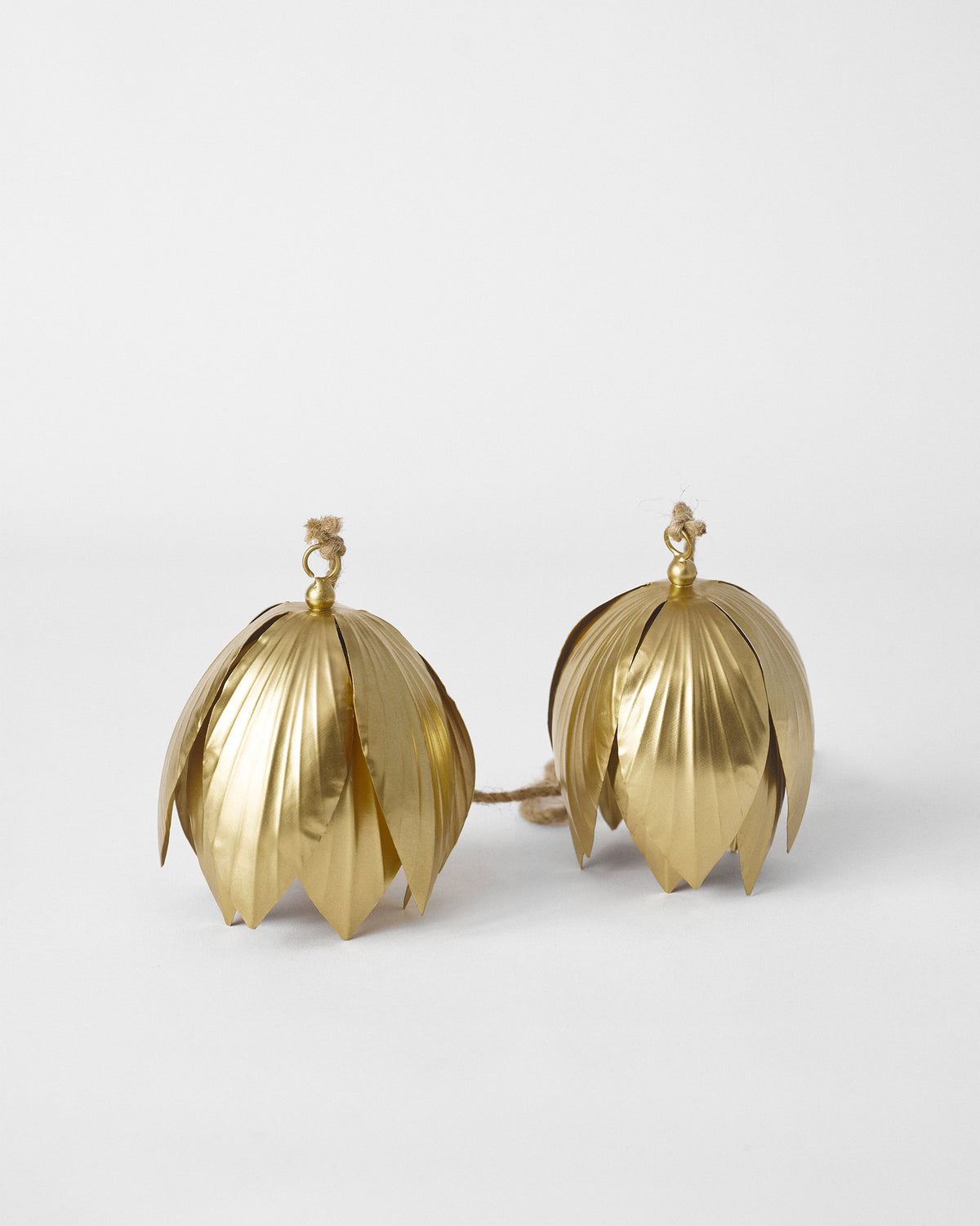 Pair of gold lotus-petal bells linked by natural jute cord on white.