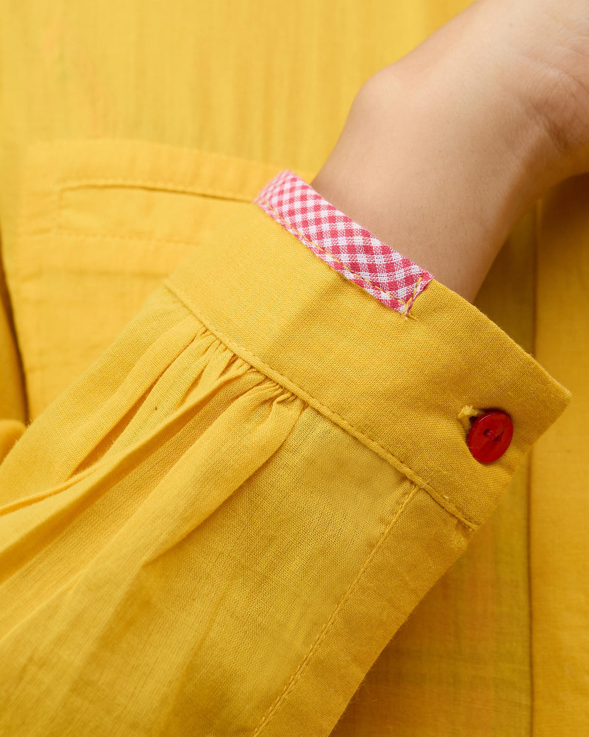 Close-up of Aurora Dress cuff with a red button and check lining.